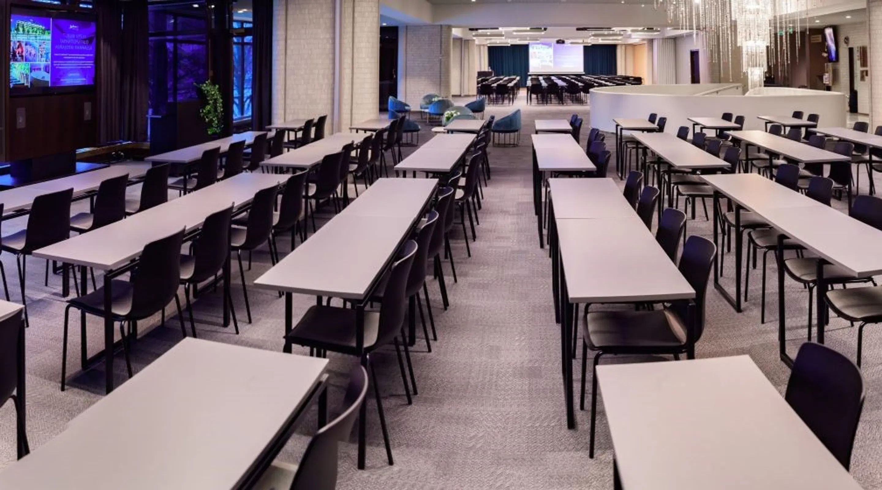 Spacious conference room with white tables arranged in rows. An auditorium and crystal chandelier visible in the background.