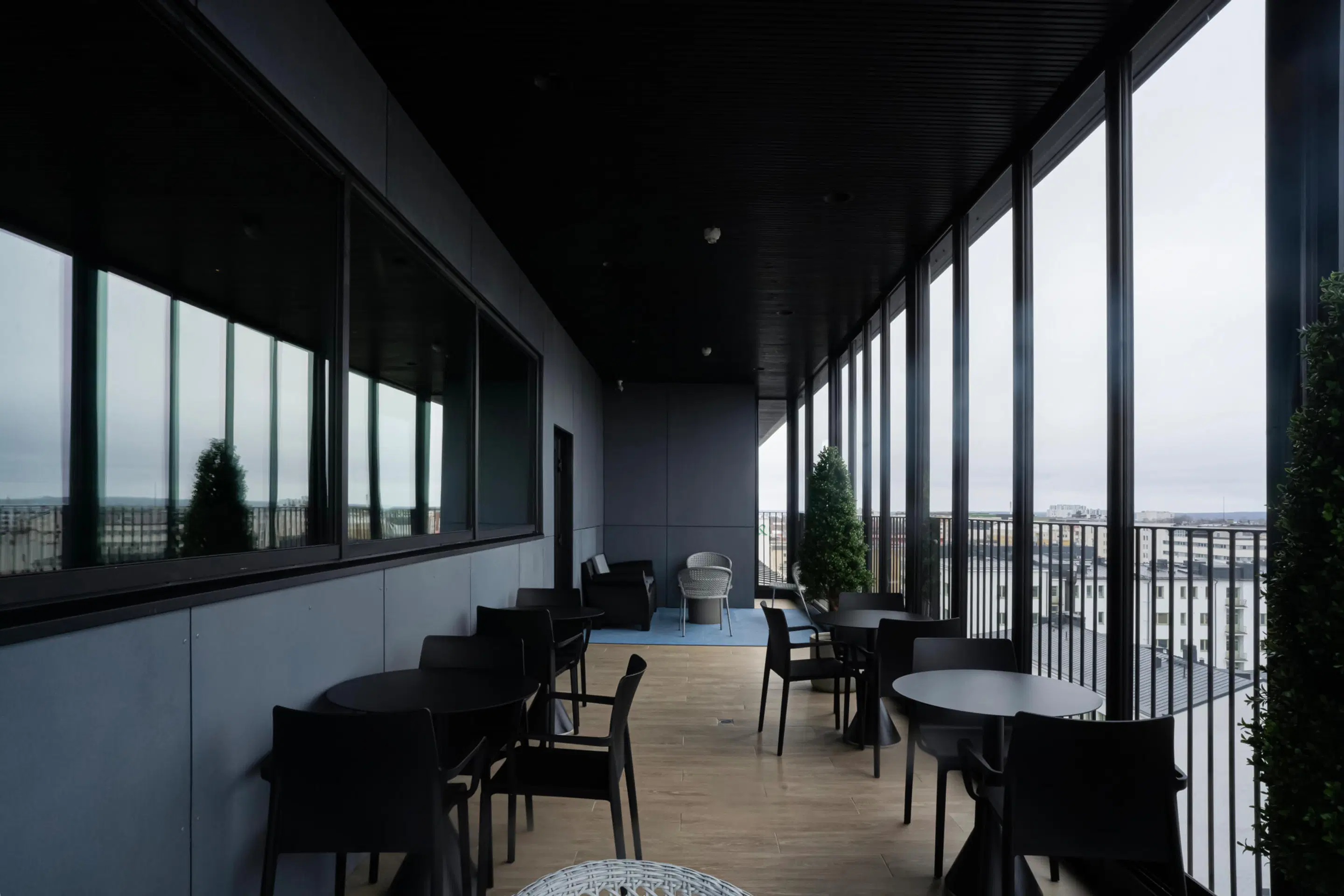Modern terrace high in a building with black tables and chairs, wooden flooring and panoramic city views. Level walkway throughout.
