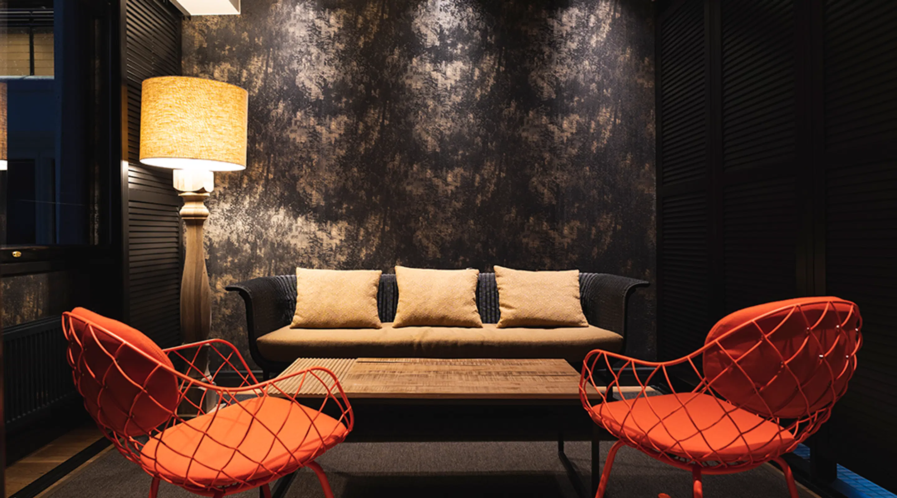 Elegant inredd loungeområde med svart soffa med beige kuddar, två klarröda designstolar och ett träsoffbord.