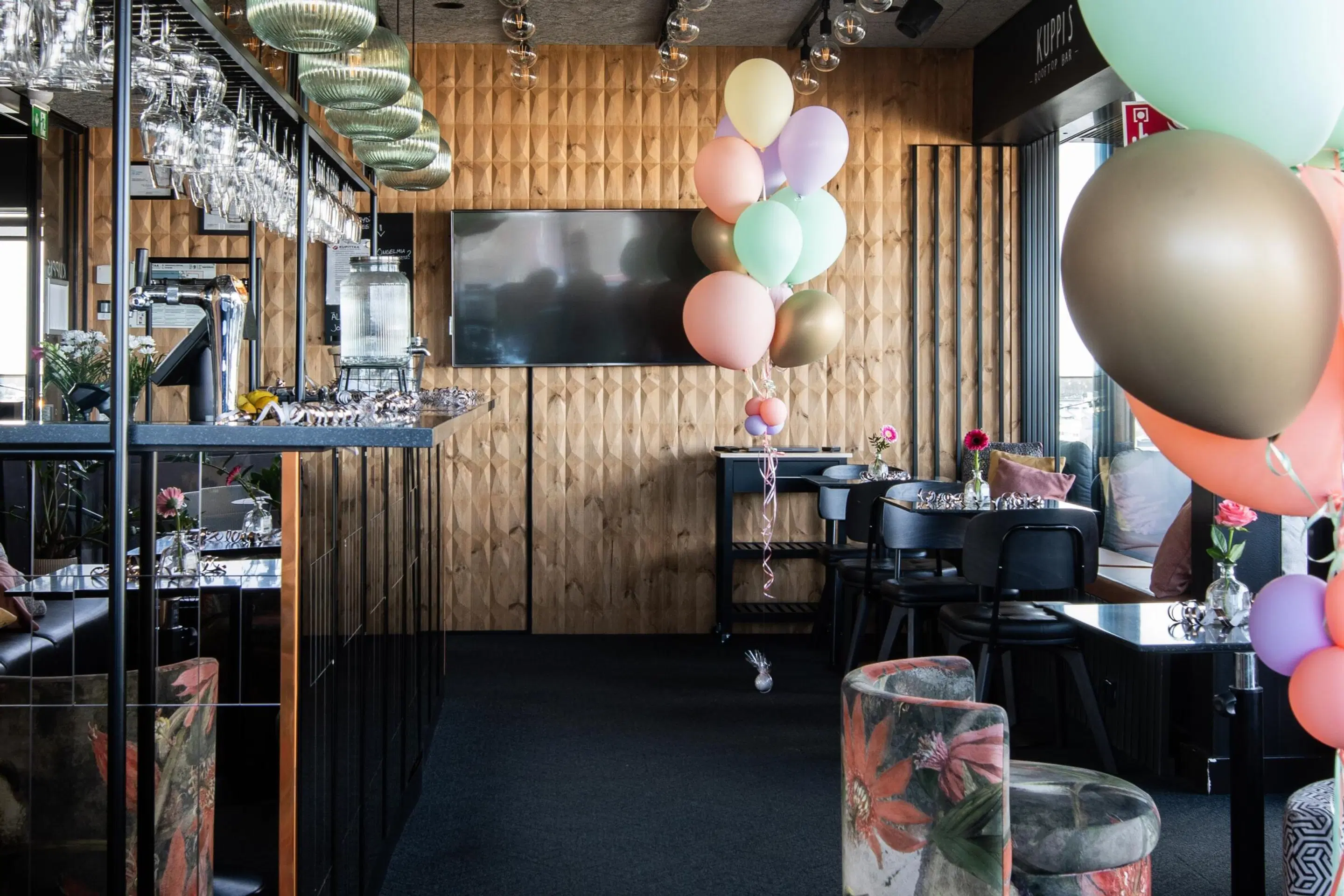Juhlakoristeltu Kuppis Rooftop Bar, jossa baaritiski vasemmalla ja pöytiä oikealla. Ilmapalloja koristeena.