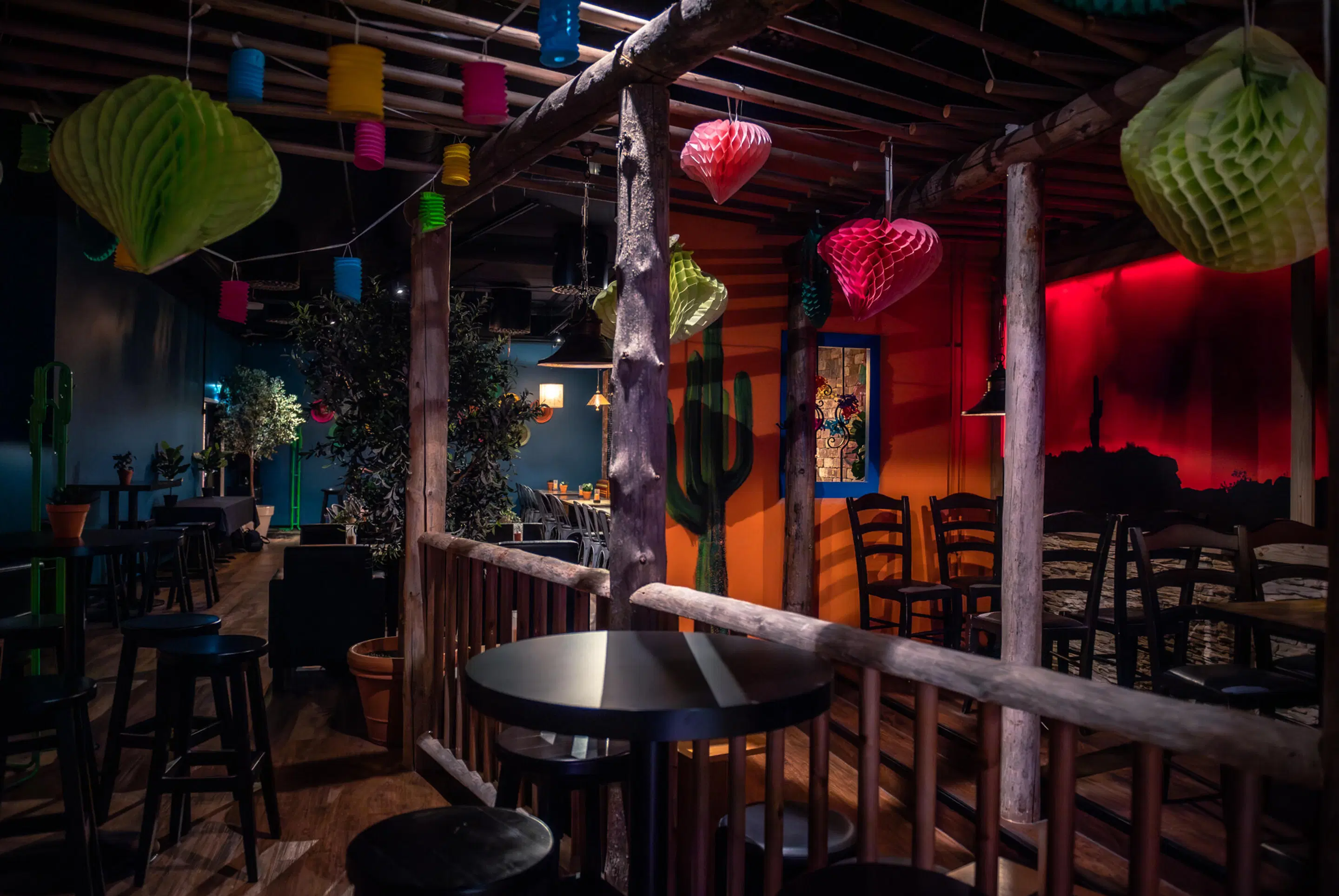 Colorfully decorated restaurant with Mexican-style elements, wooden pillars and hanging paper decorations. Wooden floor with tables of various sizes.