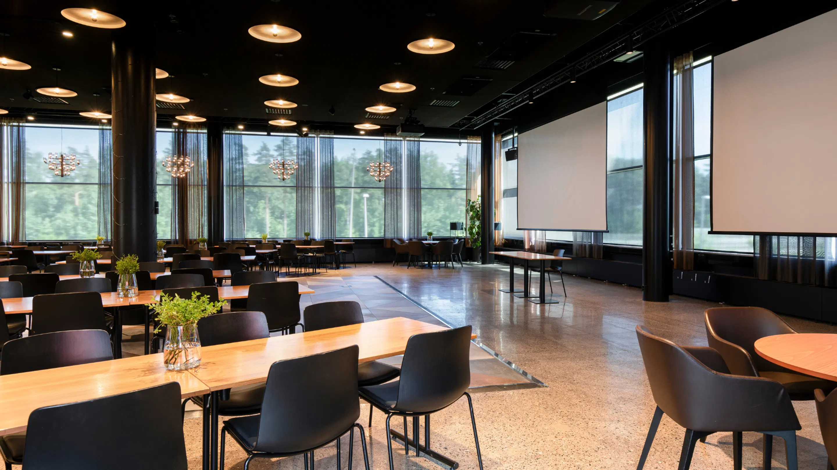 Modern conference room with large windows and projection screen. Wooden tables, black chairs, and smooth stone floor.