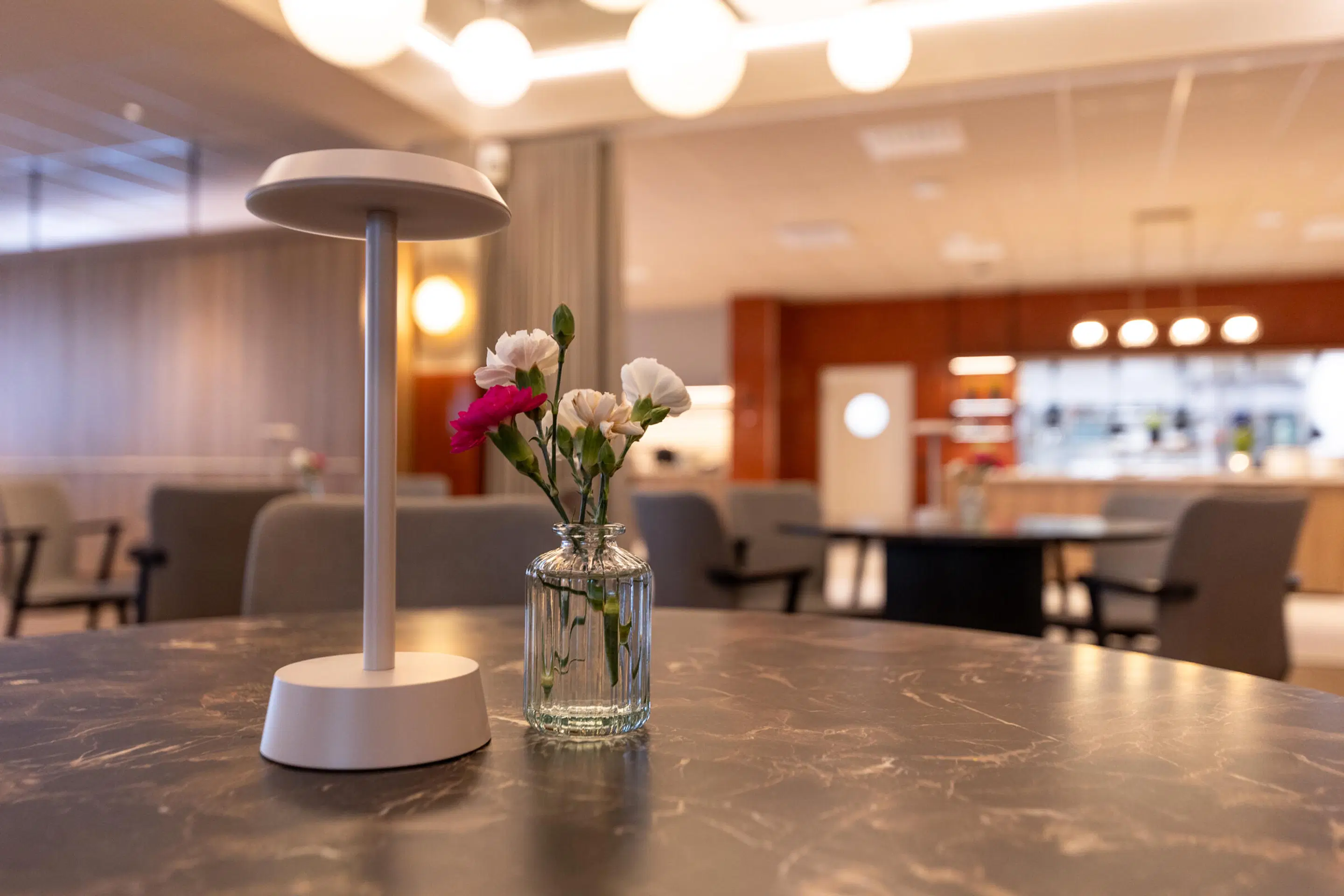 Moderni lounge-tila, jossa pöytiä ja matalia istuimia. Pöydät ovat eri korkeuksilla, taustavalaistus on hämärä.