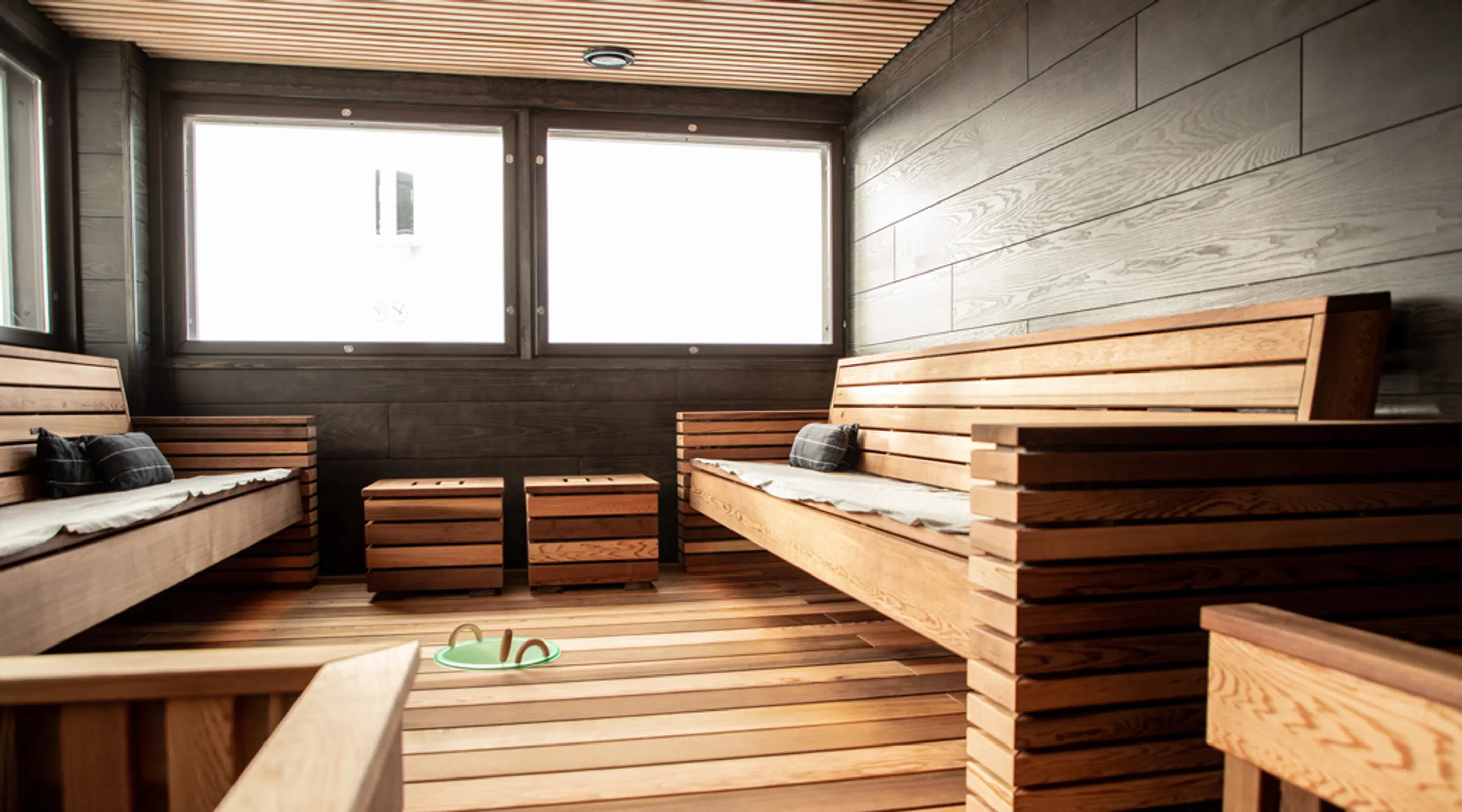 Modernisti sisustettu sauna puisilla seinäpaneeleilla, lauteilla ja lattialla. Ikkunat tuovat luonnonvaloa tilaan.