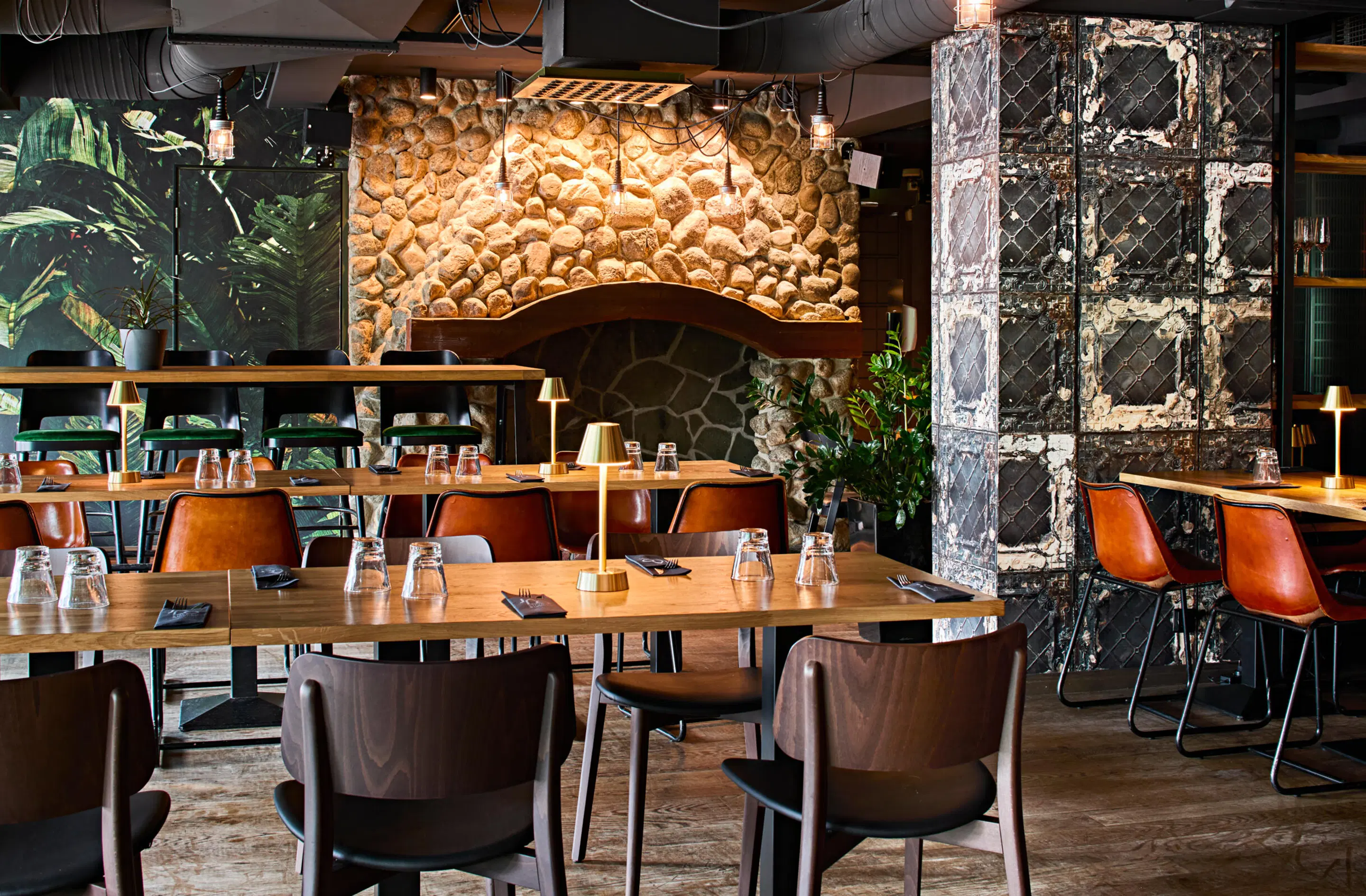 Modern restaurant with stone wall and plant wall theme. Wooden tables, leather chairs, flat wooden floor and ample space between tables.