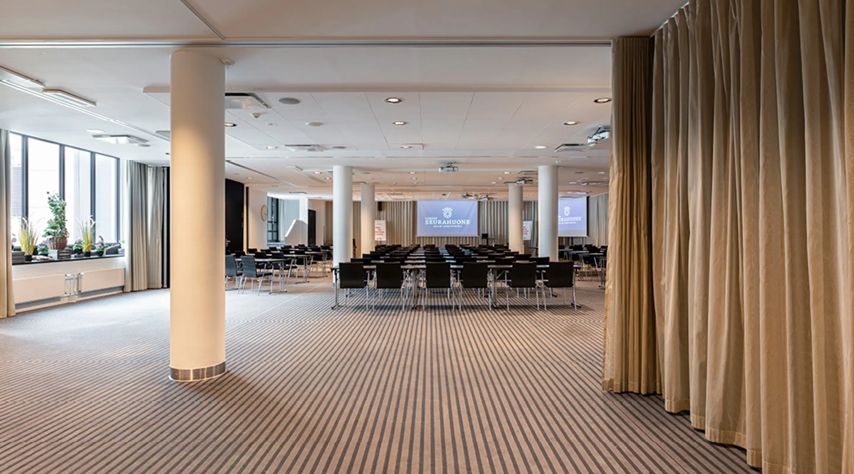 Rymlig konferenslokal med konferensbord, beige-randig matta och keramiska pelare.