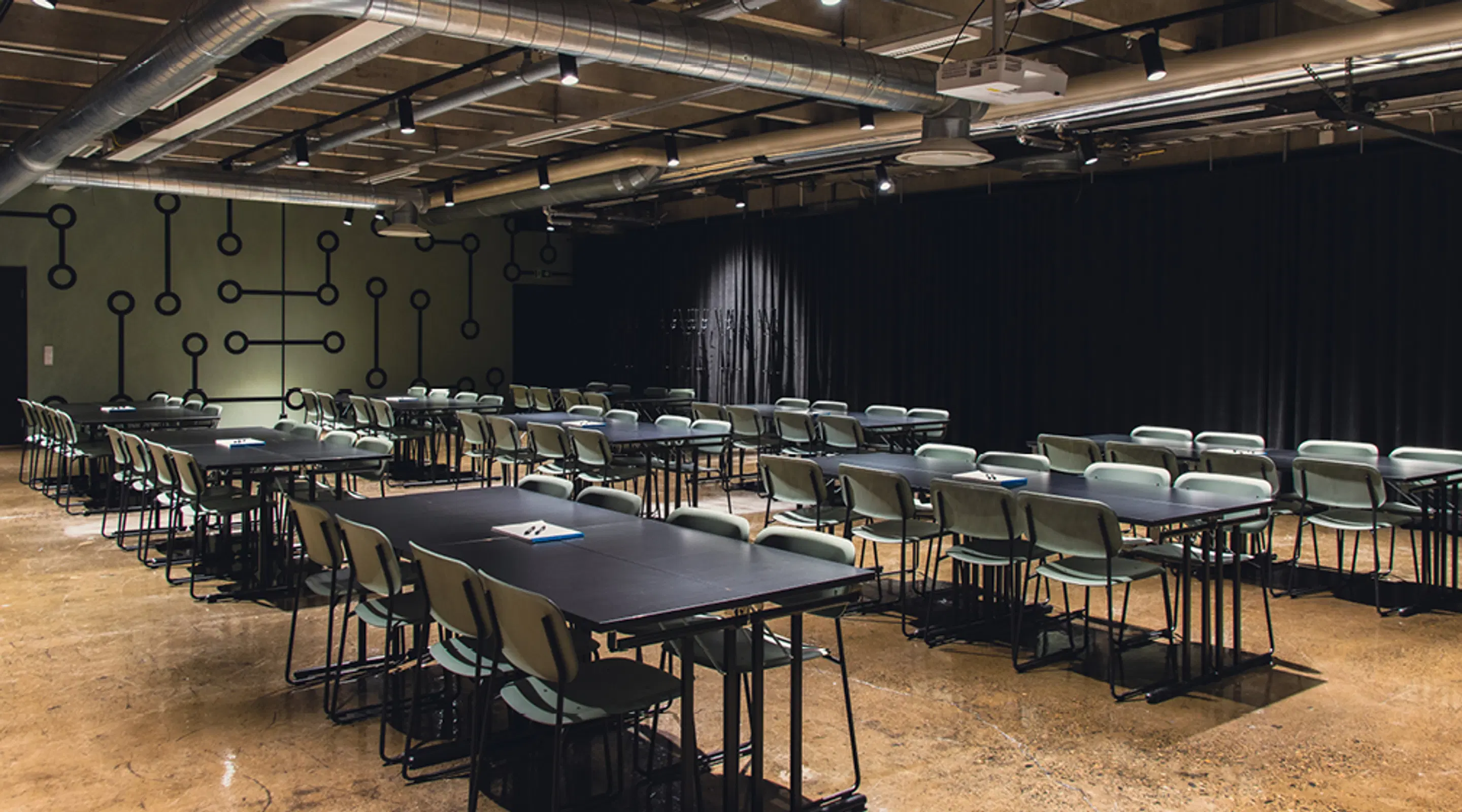 Modern conference room with black tables and gray chairs, green wall with circuit pattern and black curtain at the back.