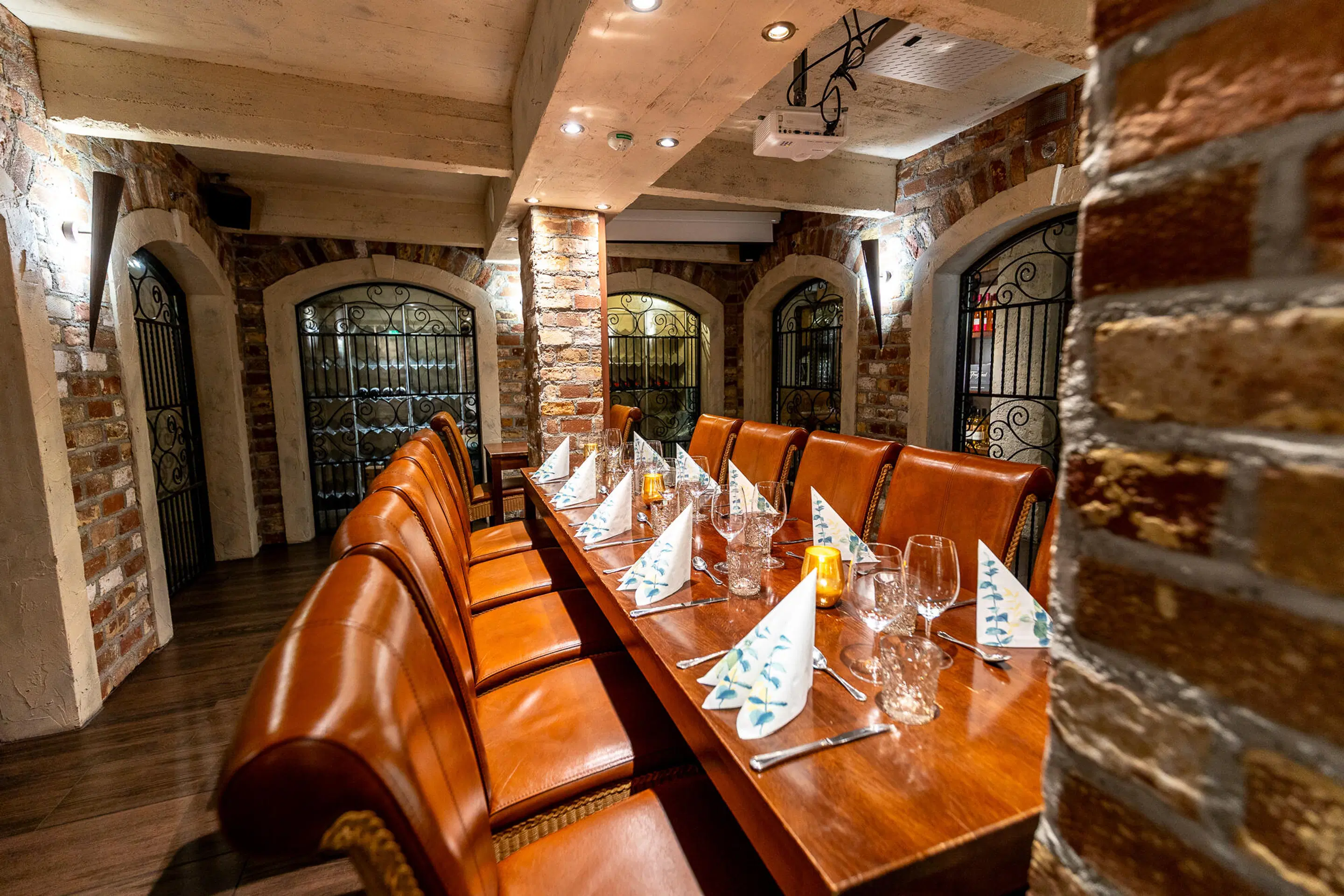 Stämningsfullt privat rum i källarrestaurang med tegelväggar, långt bord och orangea läderstolar. Genom bågformade fönster syns vinkällare.