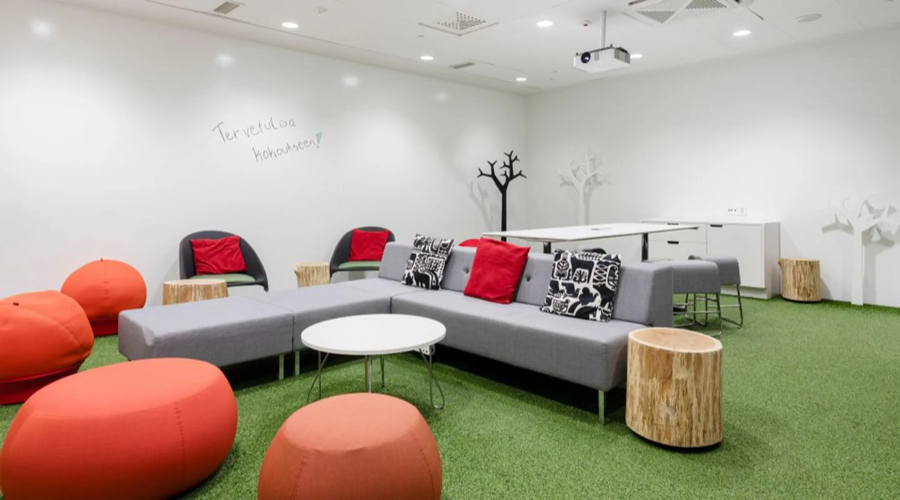 Modern office space with grey corner sofa, orange upholstered seating and green artificial grass flooring.