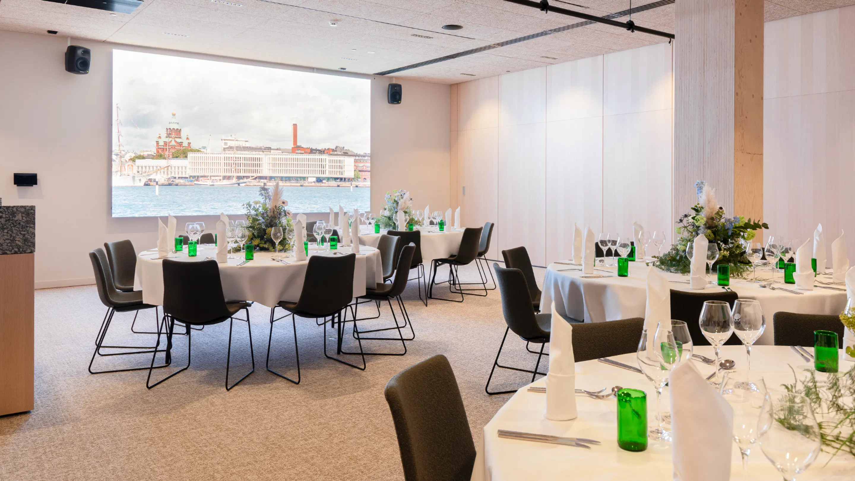Banquet room with round tables covered in white tablecloths and black chairs. Large window in background shows sea view and Helsinki's Uspenski Cathedral.
