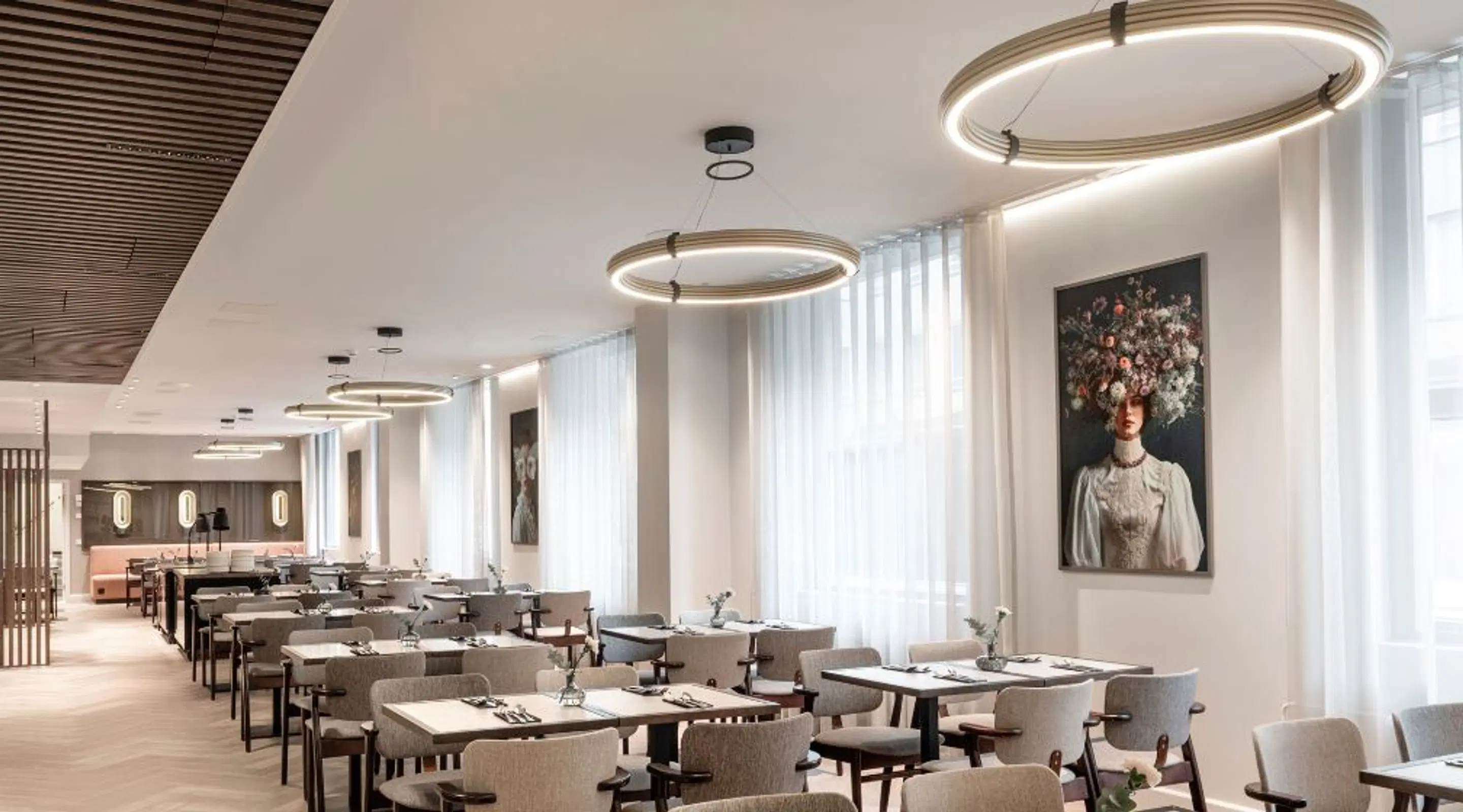 Bright restaurant with circular ceiling lights, grey chairs and white tables. Floral artwork on the walls.
