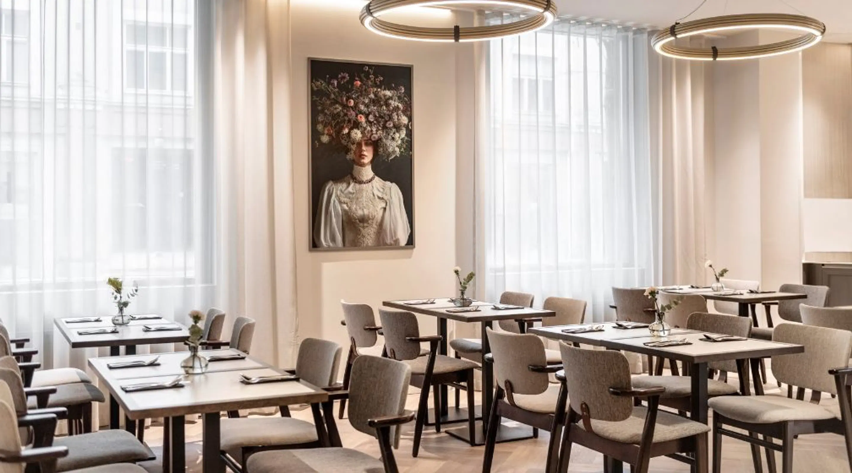Bright restaurant with light-colored tables and chairs, decorative art on the wall and two circular ceiling lights.