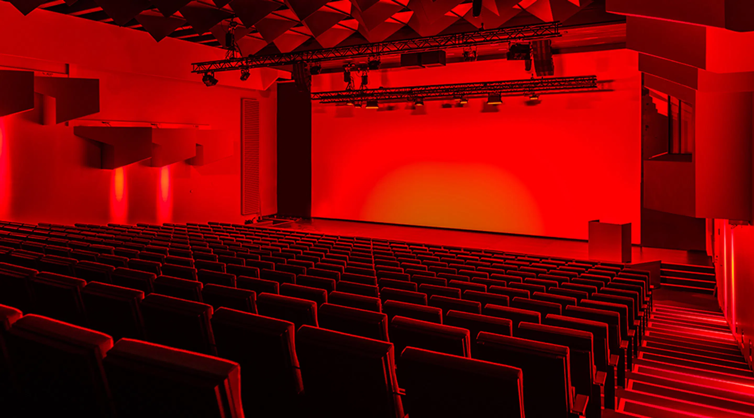 Suuri auditorio, jossa rivit istumapaikkoja laskevat tasaisesti kohti näyttämöä punaisessa valaistuksessa.