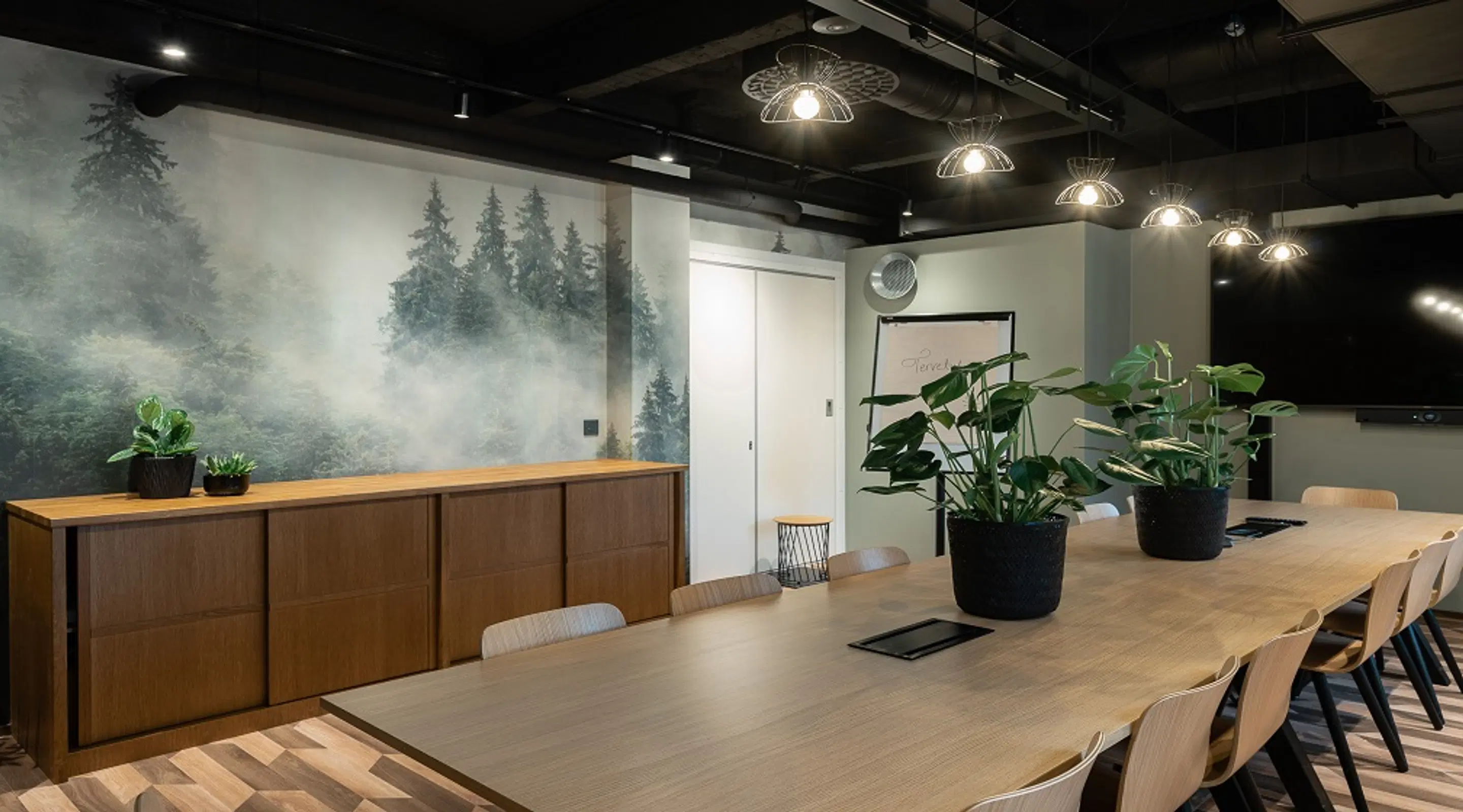 Modern meeting room with wooden table, potted plants, and large forest-themed wall mural.