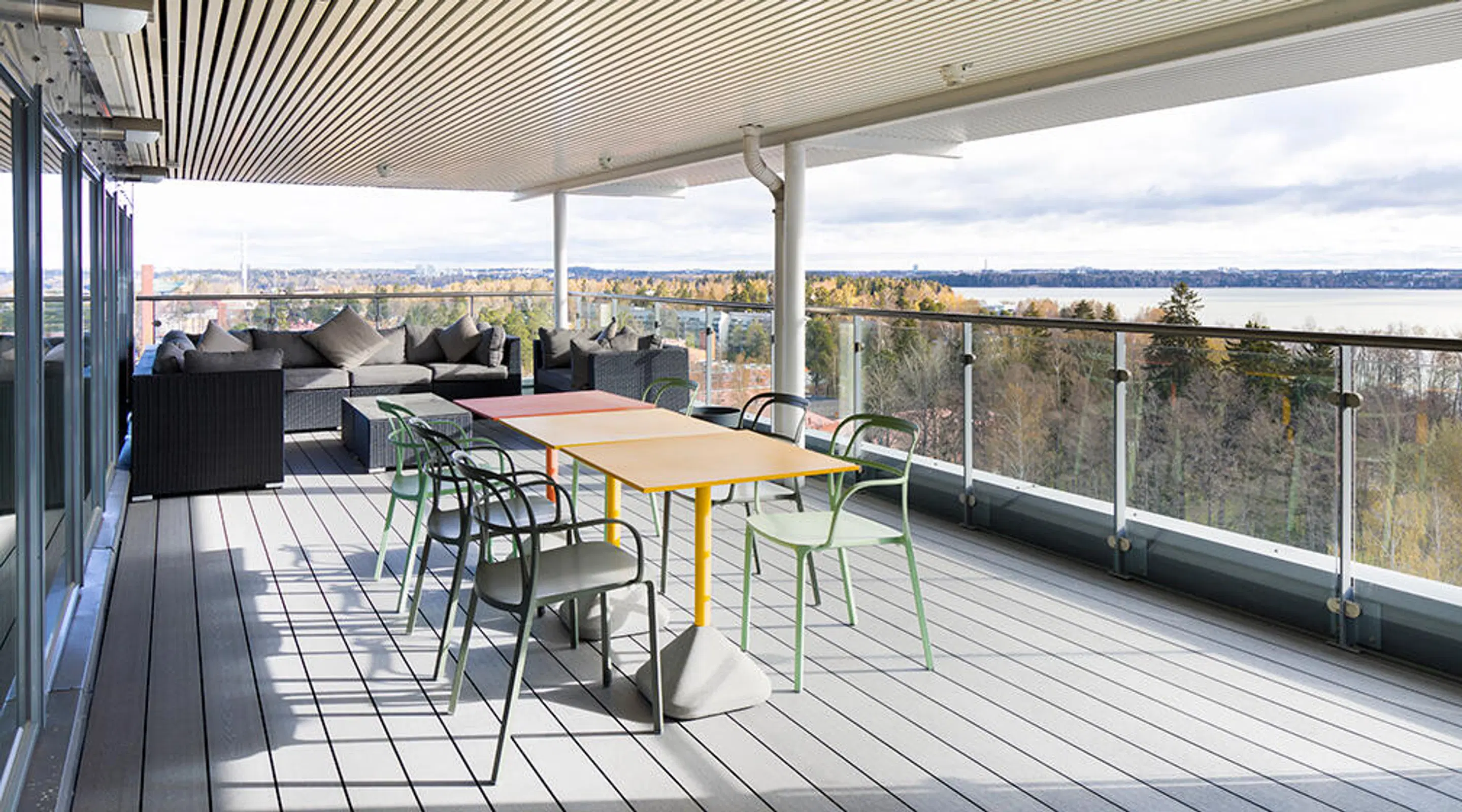 Spacious terrace with colorful tables, chairs and a lounge area. Beautiful view overlooking a lake and autumn forest landscape.