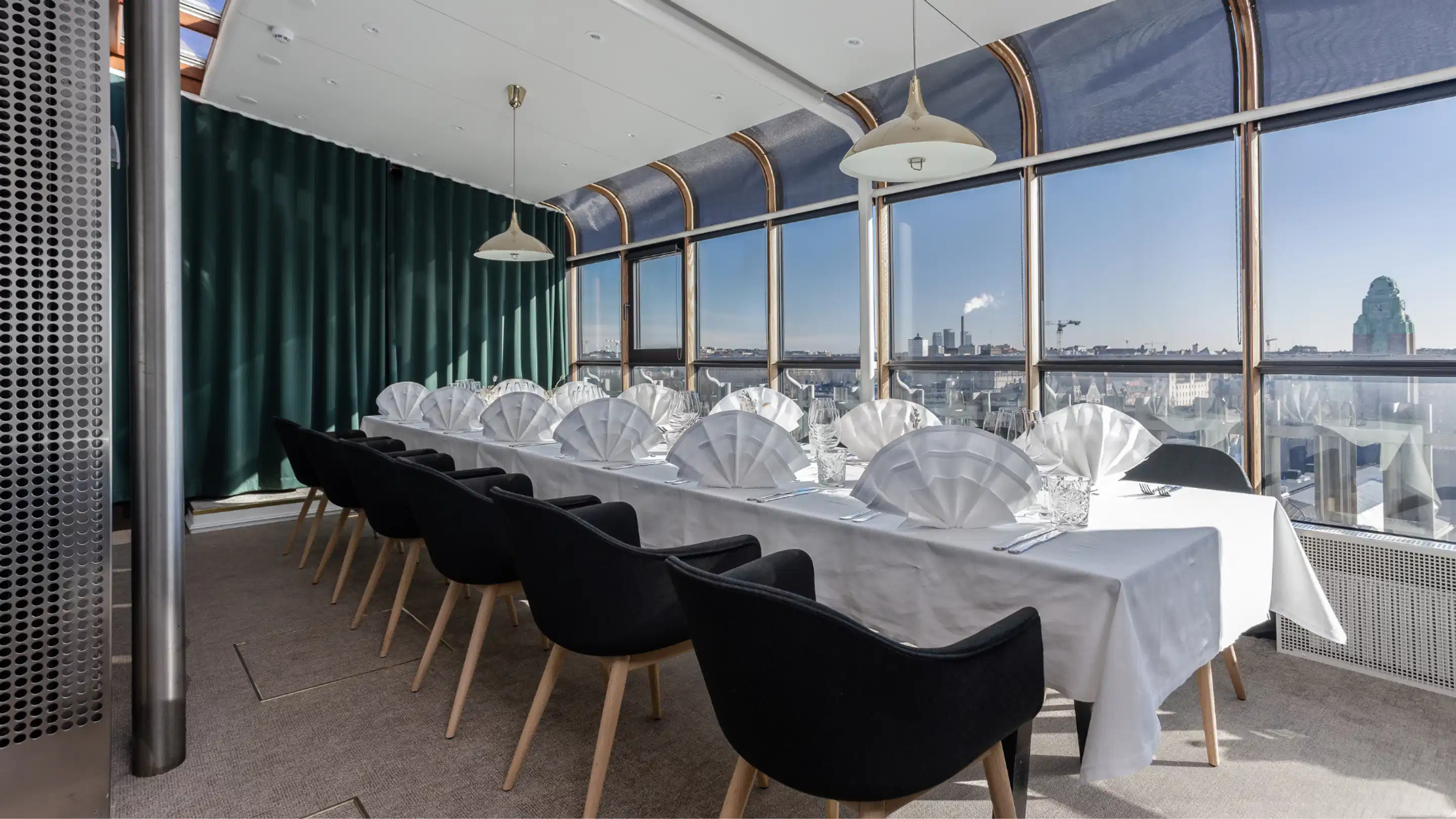 Elegant dukat långbord i restaurangavdelning med panoramafönster. Svarta stolar, vit duk och stadsutsikt i bakgrunden.