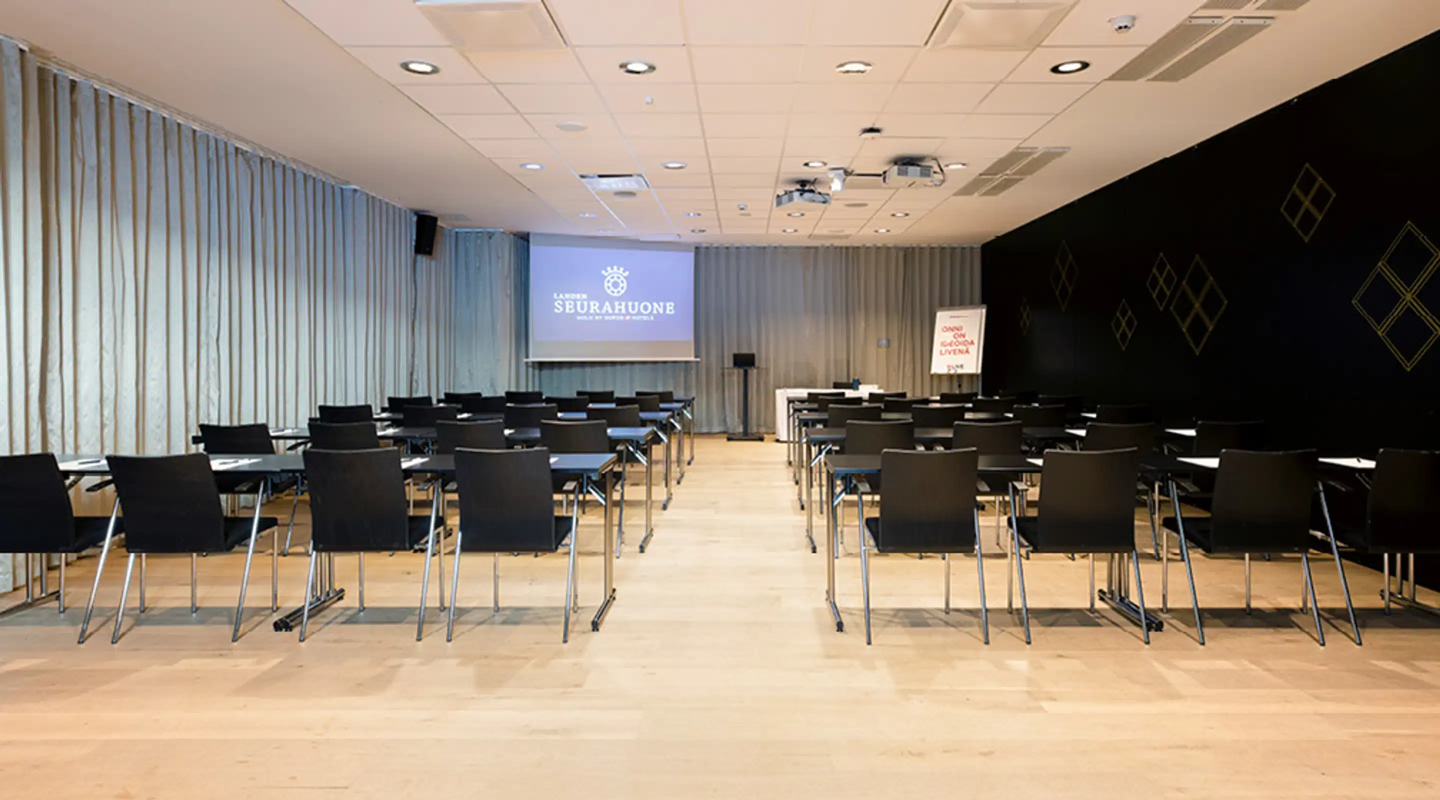 Auditorium med rader av svarta stolar på ljust golv, mittgång mellan stolsraderna.