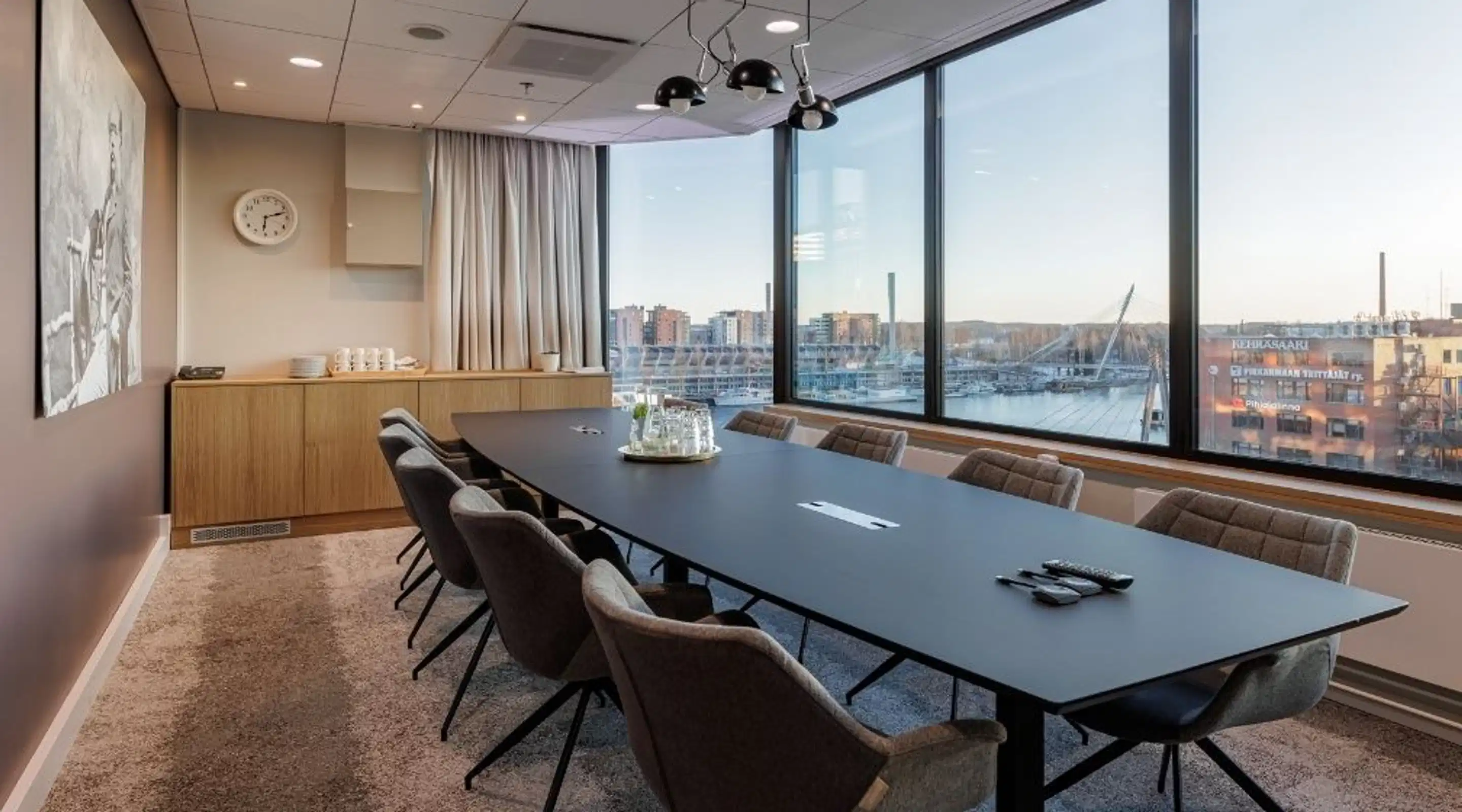 Modern conference room with a long black table, gray chairs, and large windows overlooking a marina area.