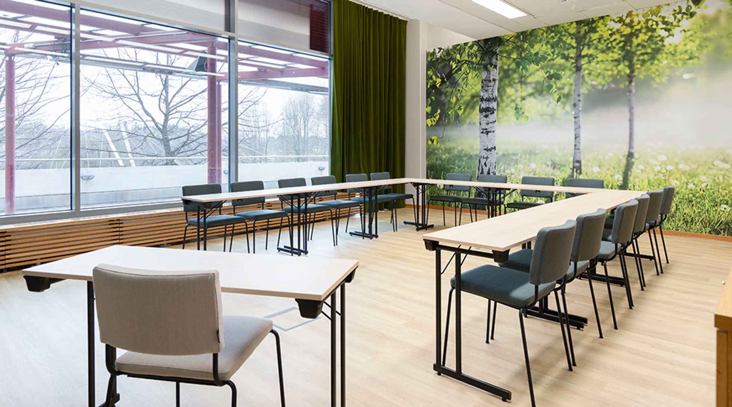Bright meeting room with wooden floor, birch forest wall mural, long tables arranged in U-shape, and winter landscape visible through windows.