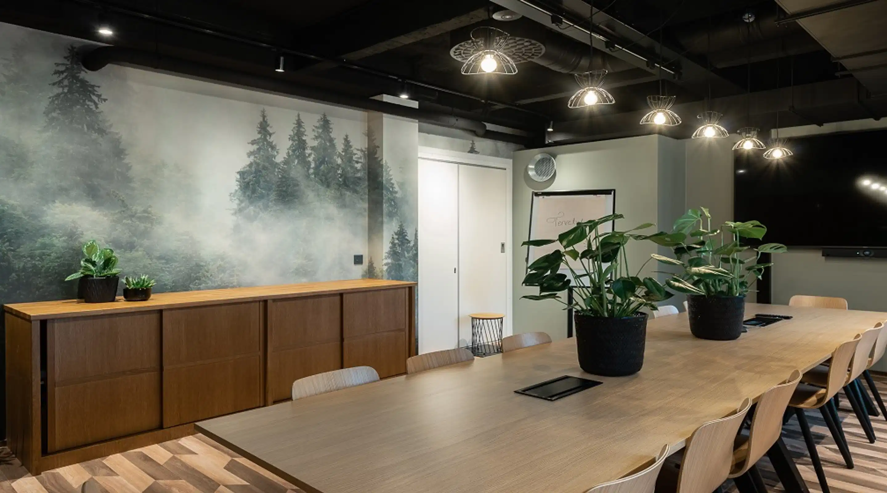 Modern meeting room with wooden table, potted plants, and large forest-themed wall mural.