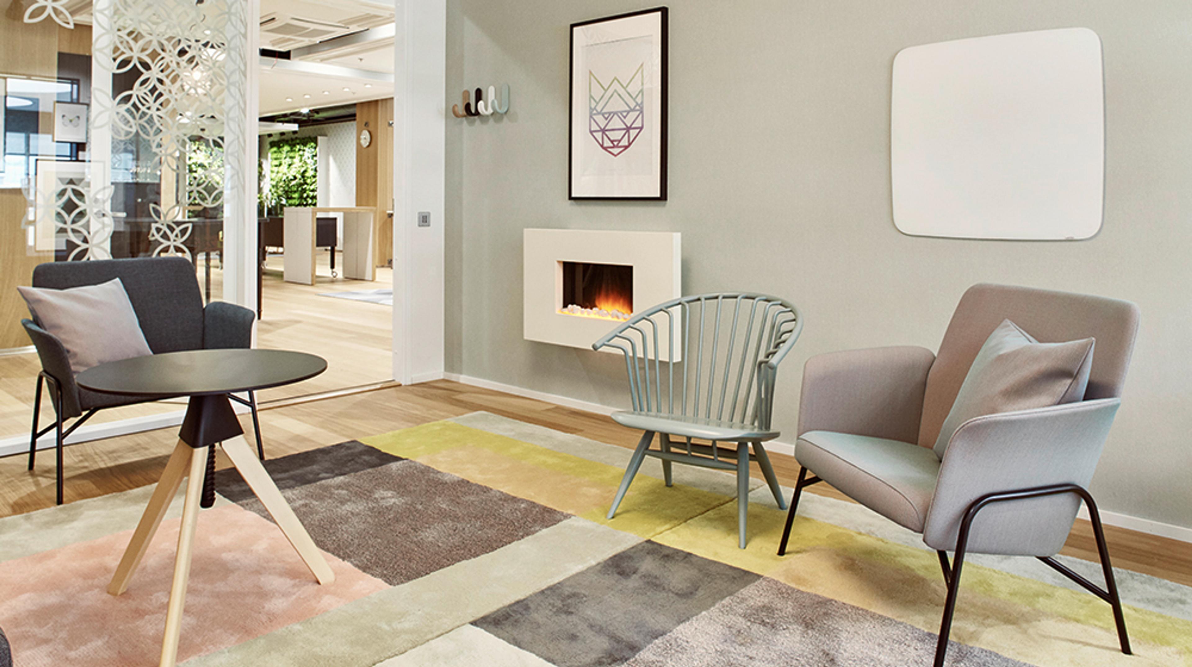 Modernisti sisustettu oleskelutila, jossa on takka, erilaisia tuoleja, pyöreä pöytä ja värikäs matto. Avoin kulkuväylä viereiseen tilaan.