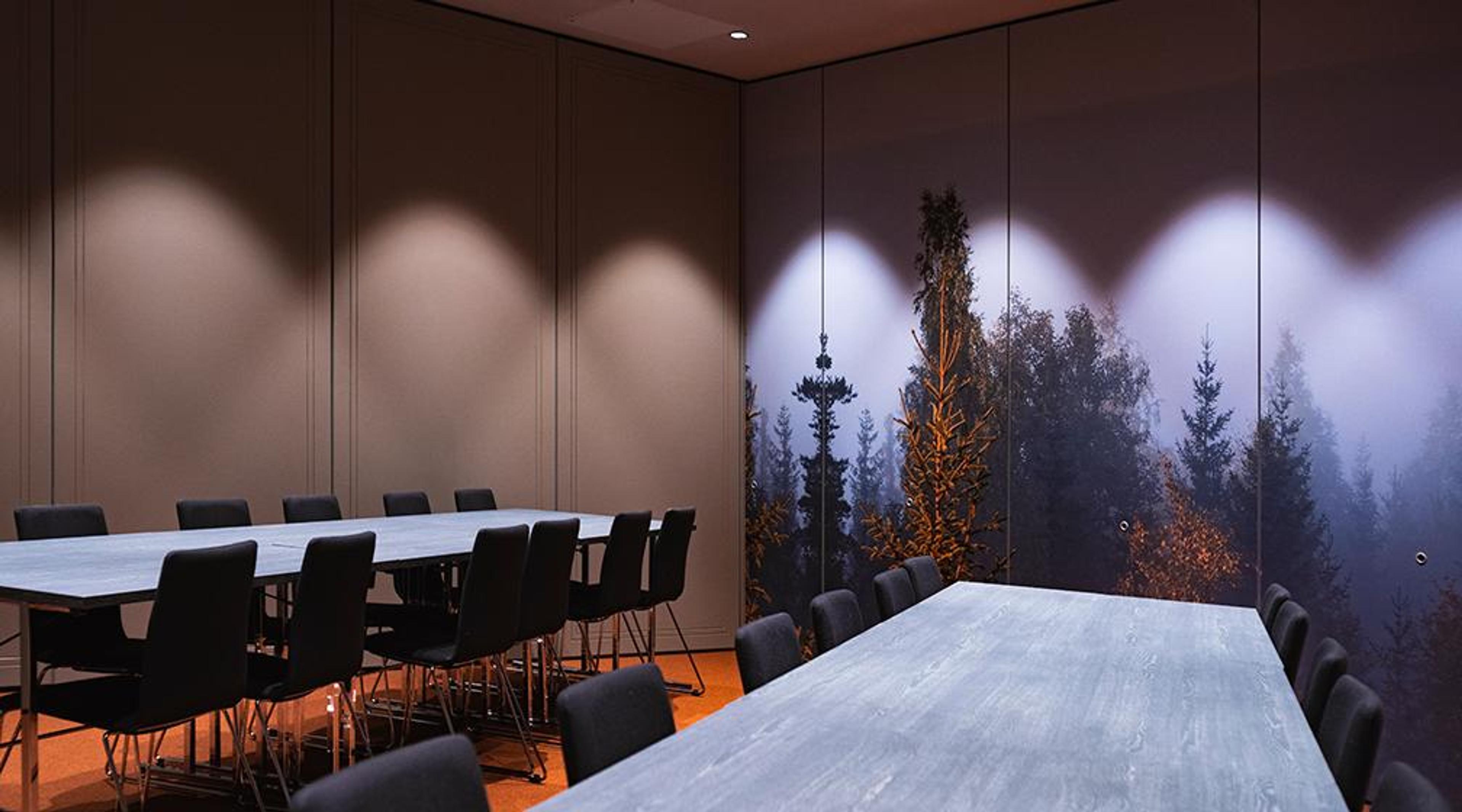 Meeting room with two long tables and black chairs. A large forest-themed mural displaying misty evergreens decorates the wall.