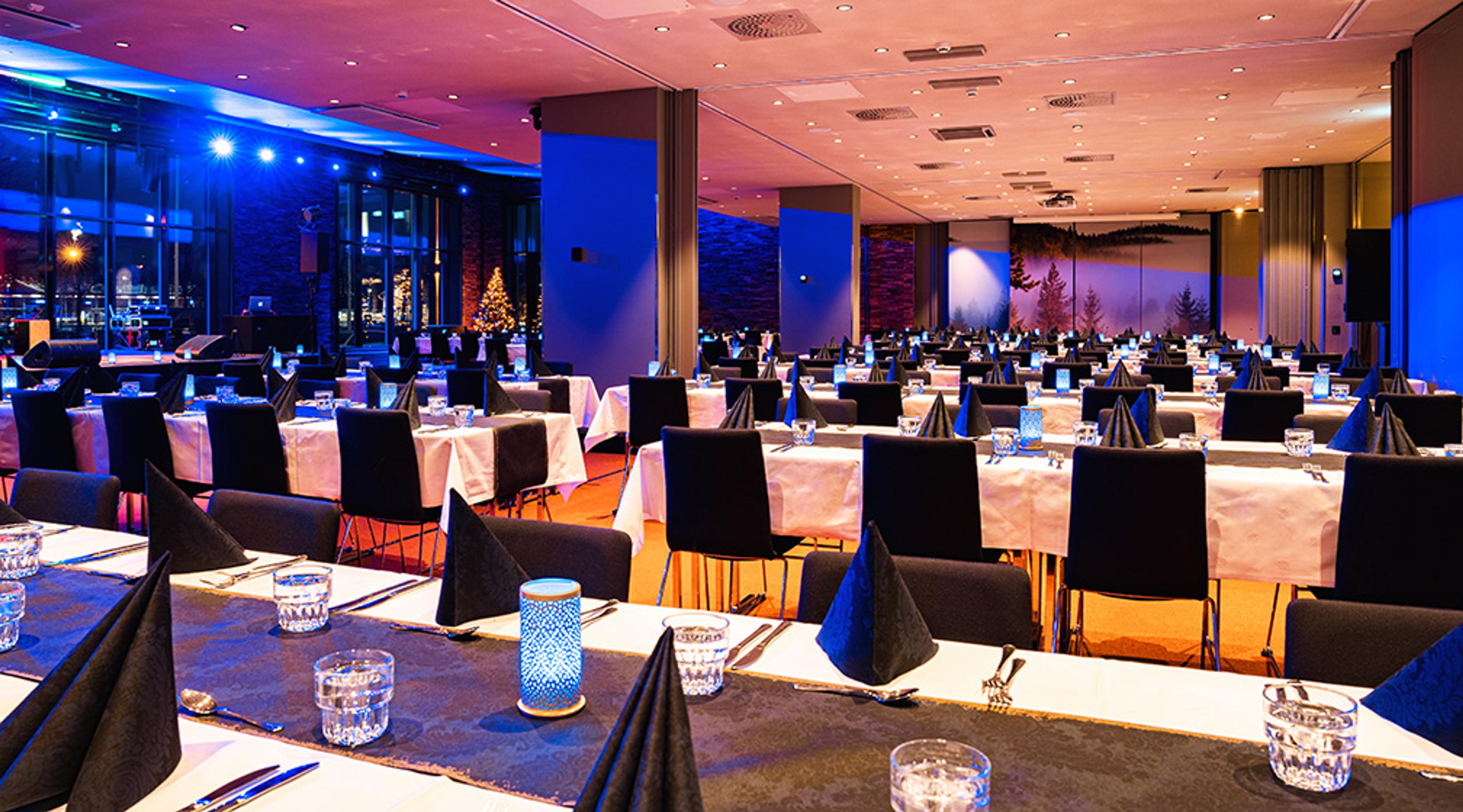 Restaurant dining area with blue lighting, black chairs, and set tables. Christmas lights and windows visible in the background.