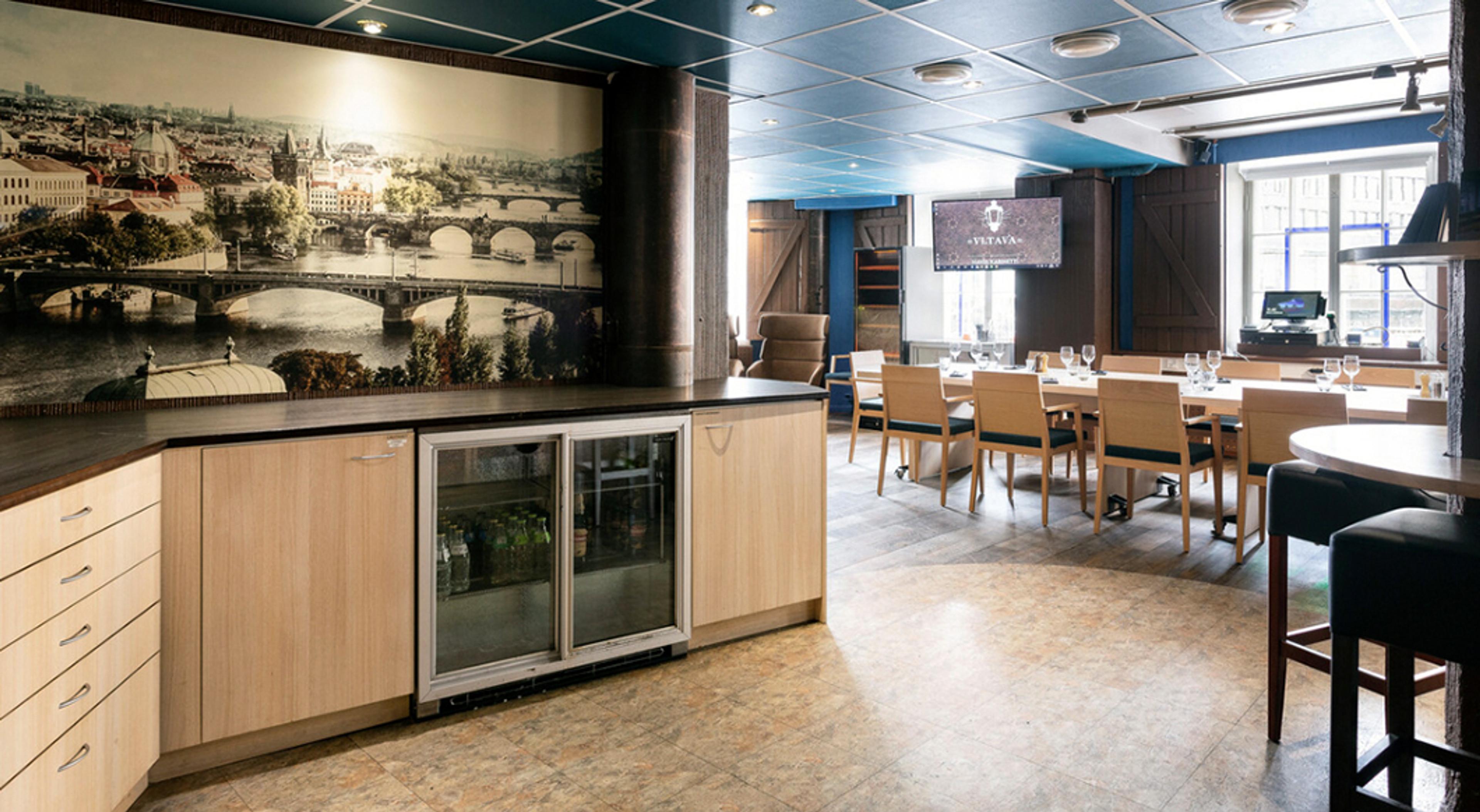 Ravintolan sisätila, jossa baaritiski ja taustalla kaupunkimaisematapetti. Tilassa on puisia ruokapöytiä ja sininen katto.