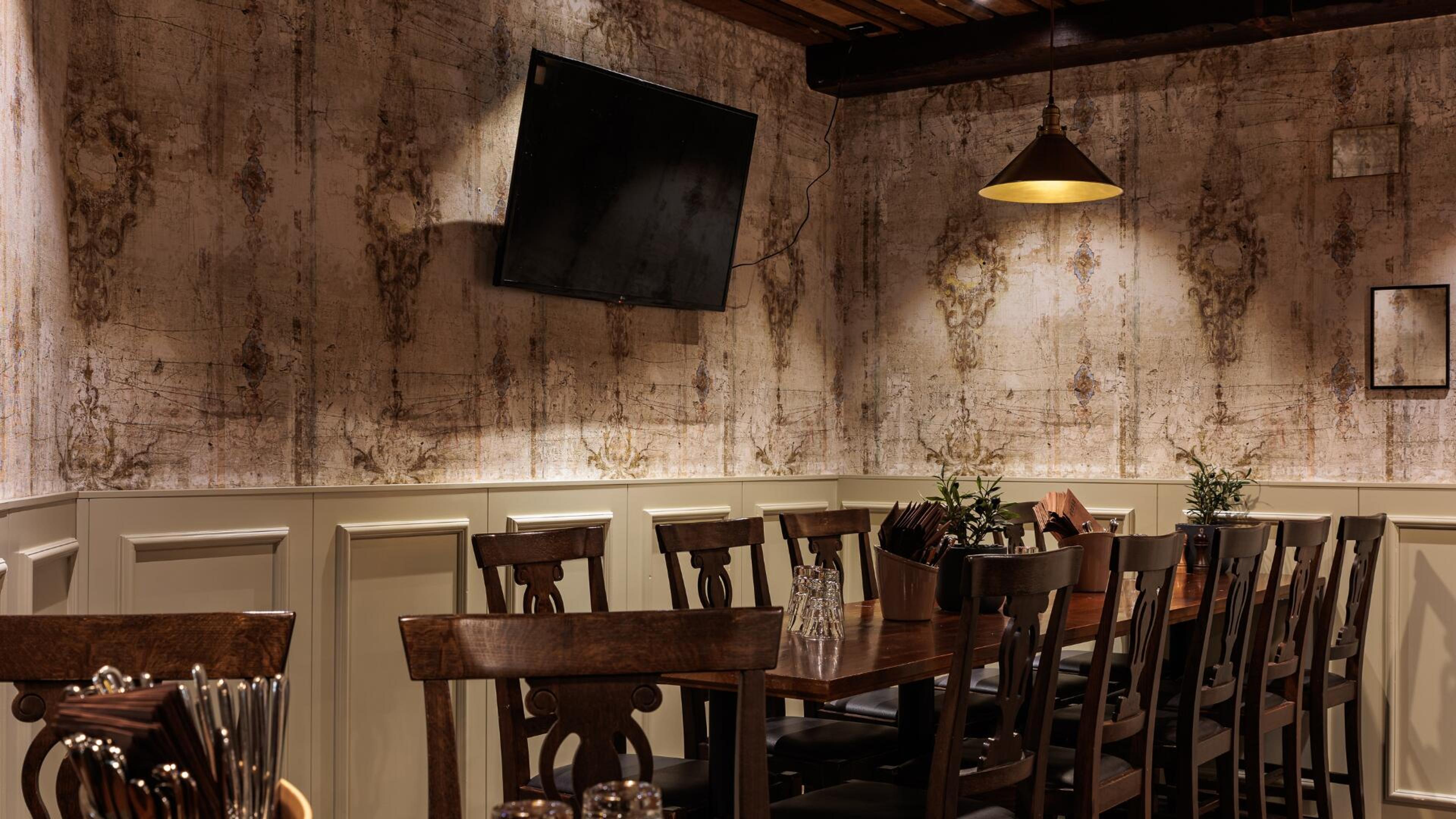 Ravintolan kabinetti, jossa pitkä puinen pöytä, tuoleja ja seinällä televisio. Seinissä vanhanaikaiset kuvioinnit ja riippuva valaisin.