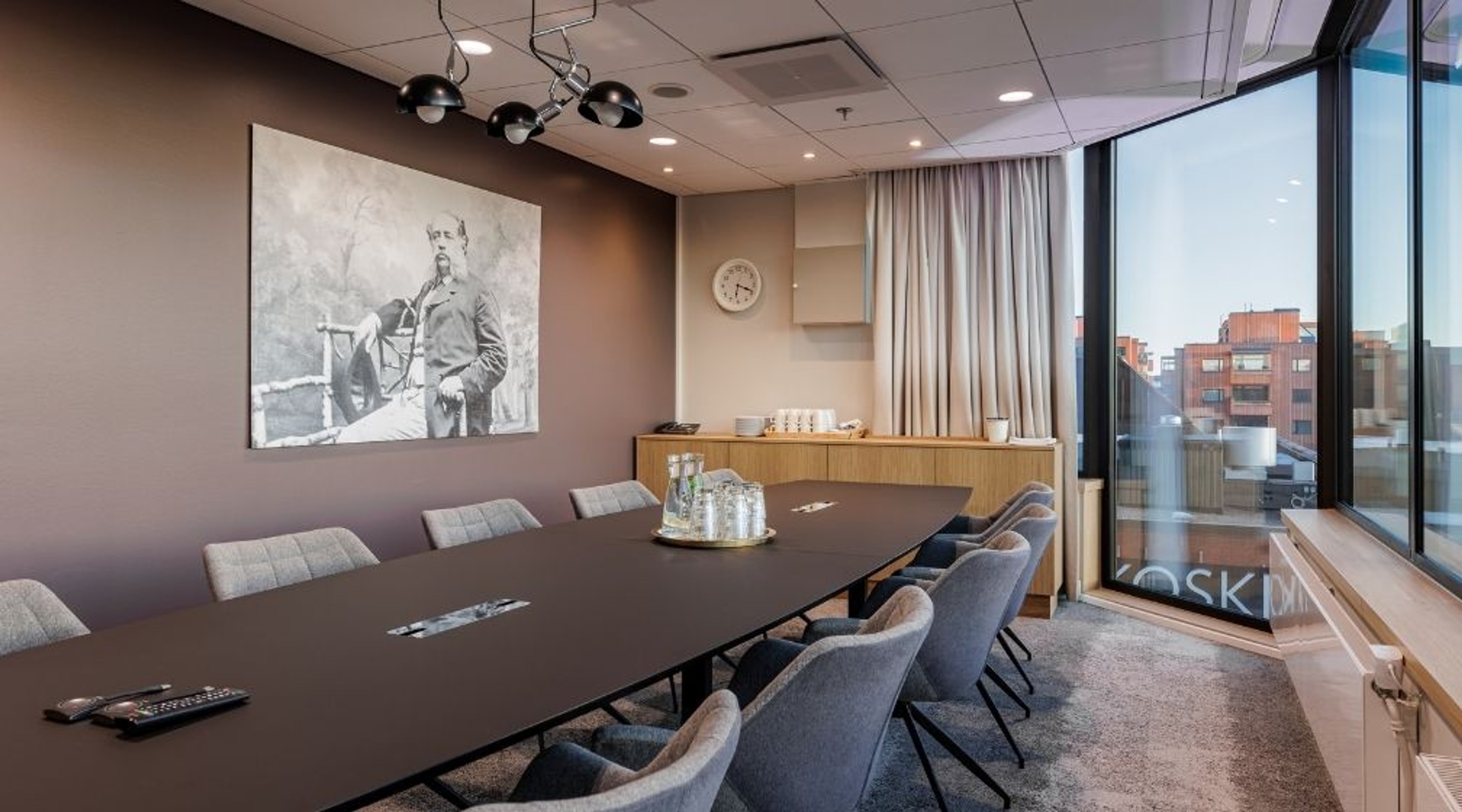 Moderni neuvotteluhuone, jossa tumma pöytä, harmaat tuolit, suuri seinäkuva ja lattiasta kattoon ikkunat tarjoavat kaupunkinäkymän.