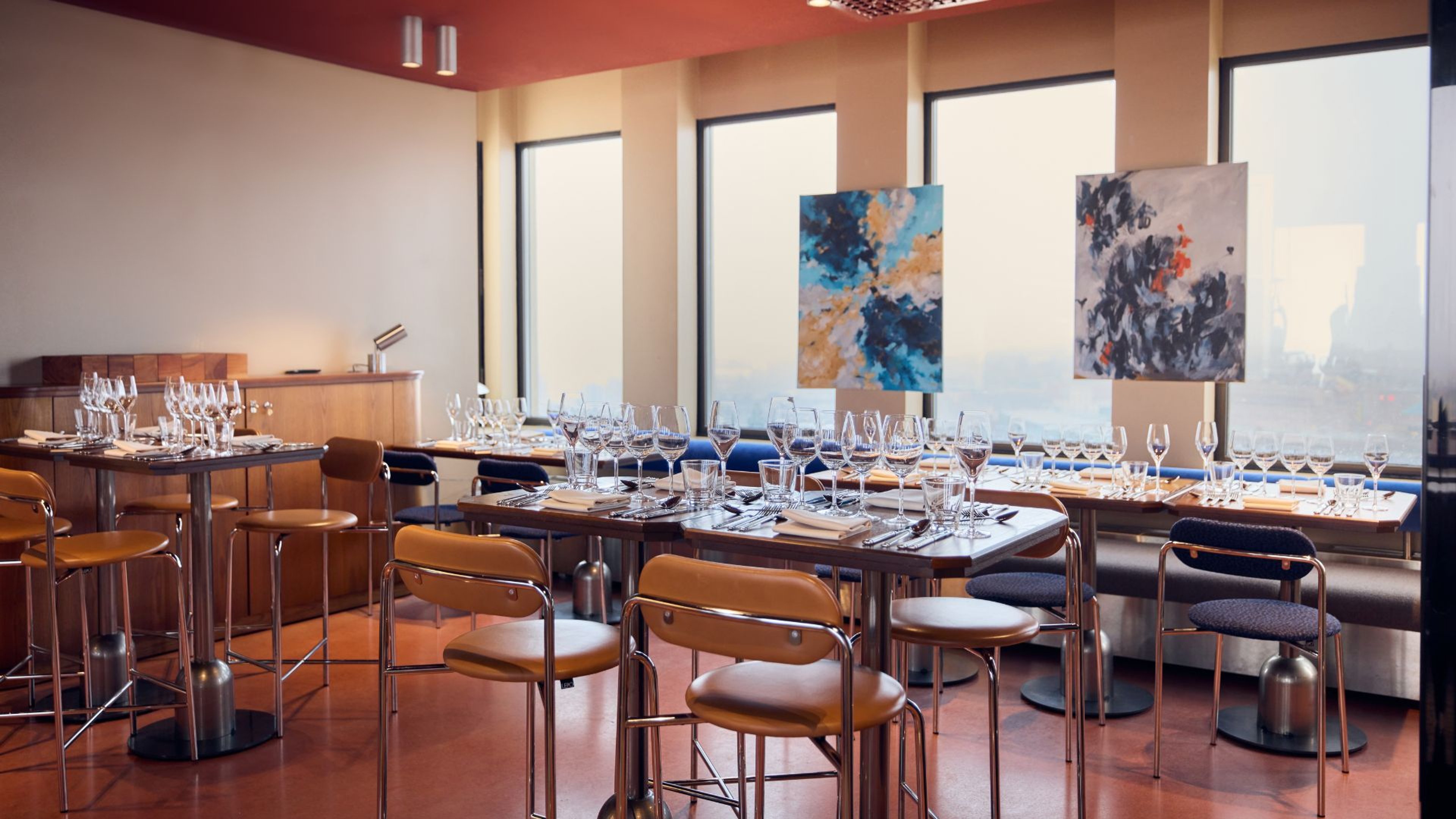 Tilava kokoushuone, jossa pitkät pöydät viinilaseilla ja asetetuilla astioilla. Seinillä moderneja taideteoksia, isot ikkunat tuovat luonnonvaloa.