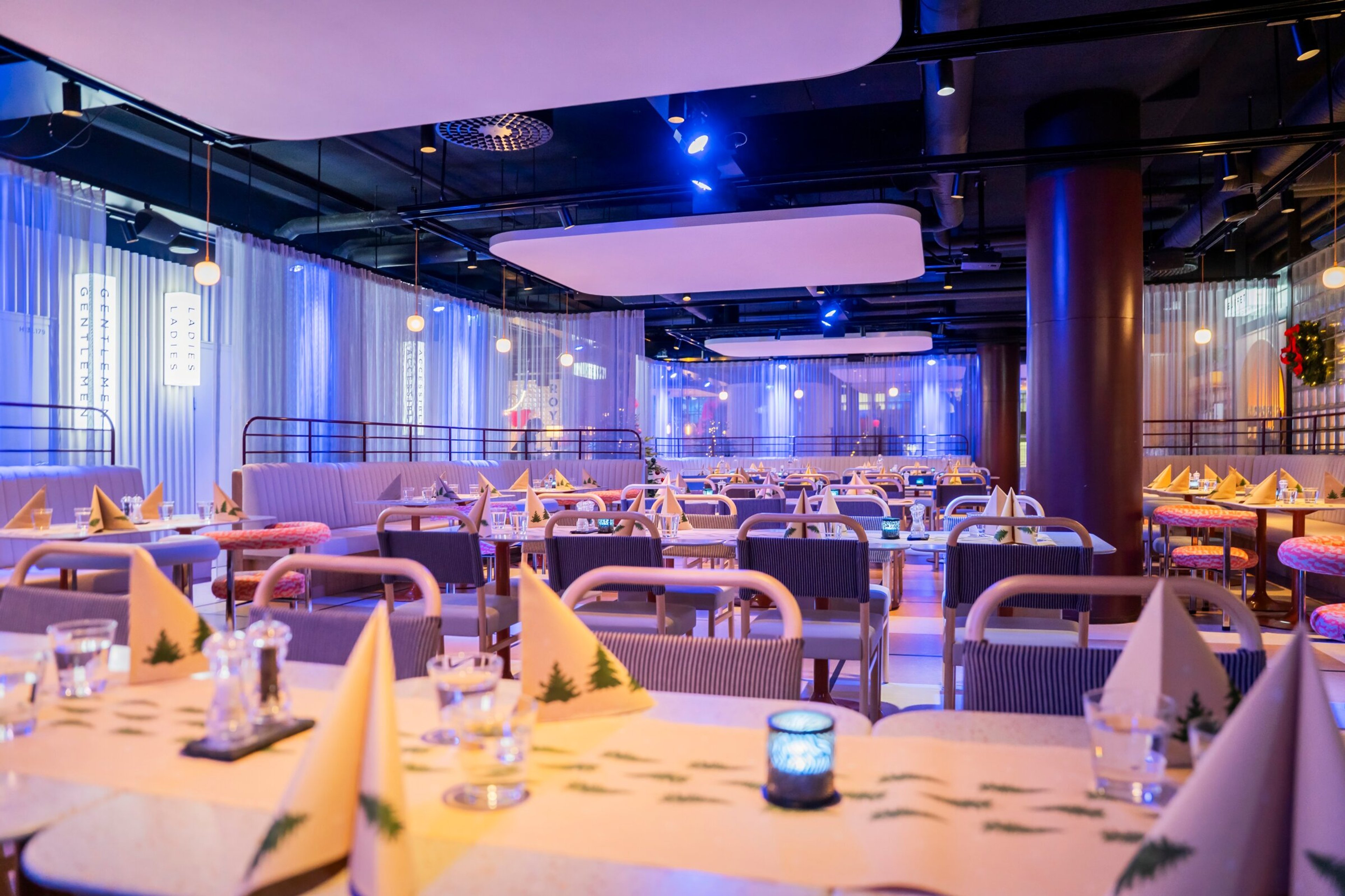 Tyylikkäästi katettu ravintolasali sinisessä valaistuksessa. Pöydät on valmisteltu juhla-ateriaa varten keltaisilla lautasliinoilla.