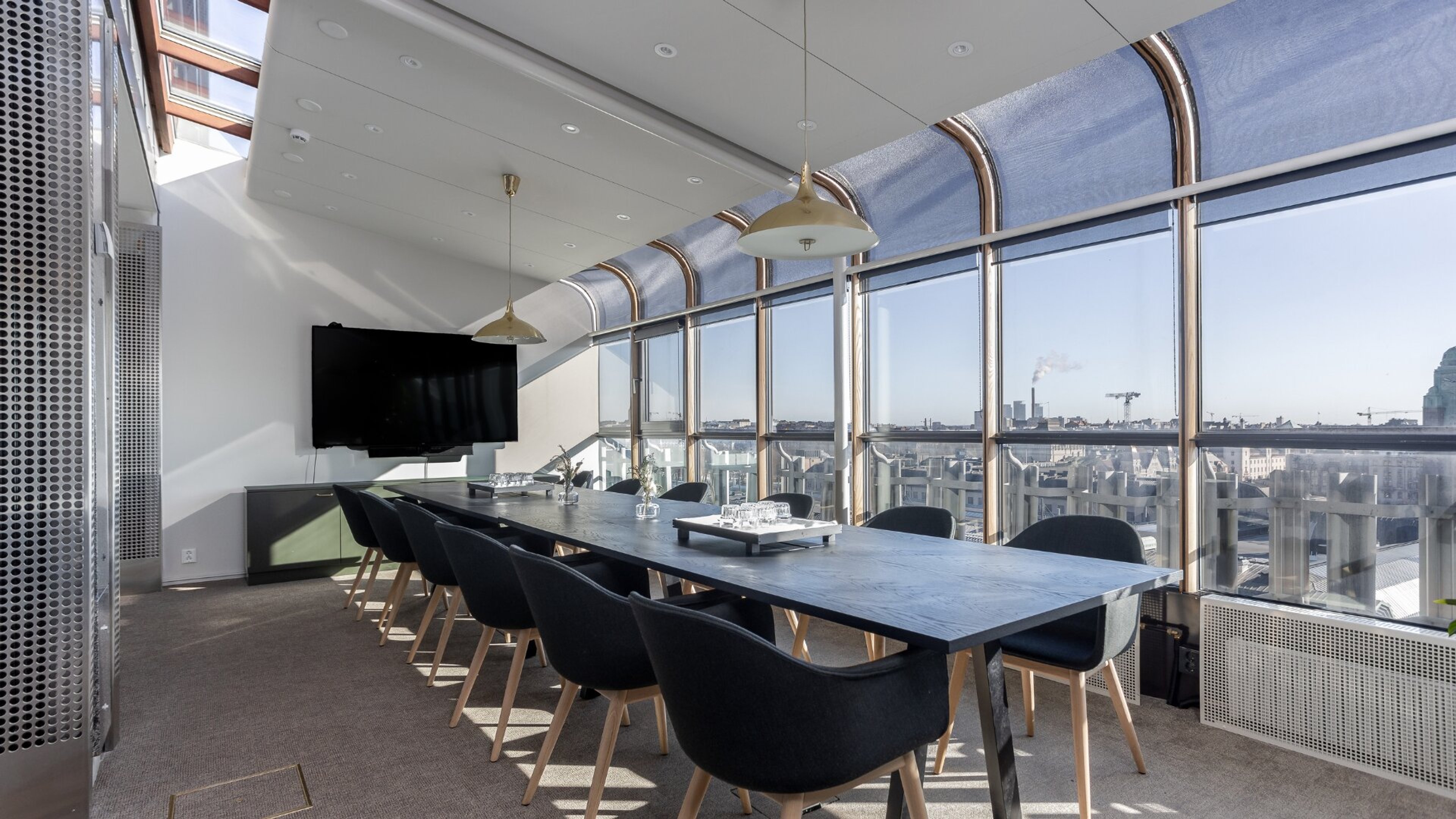 Moderni neuvotteluhuone, jossa pitkä pöytä, mustat tuolit ja panoraamaikkunat. Huoneessa on tasainen kokolattiamatto ja hyvä valaistus.