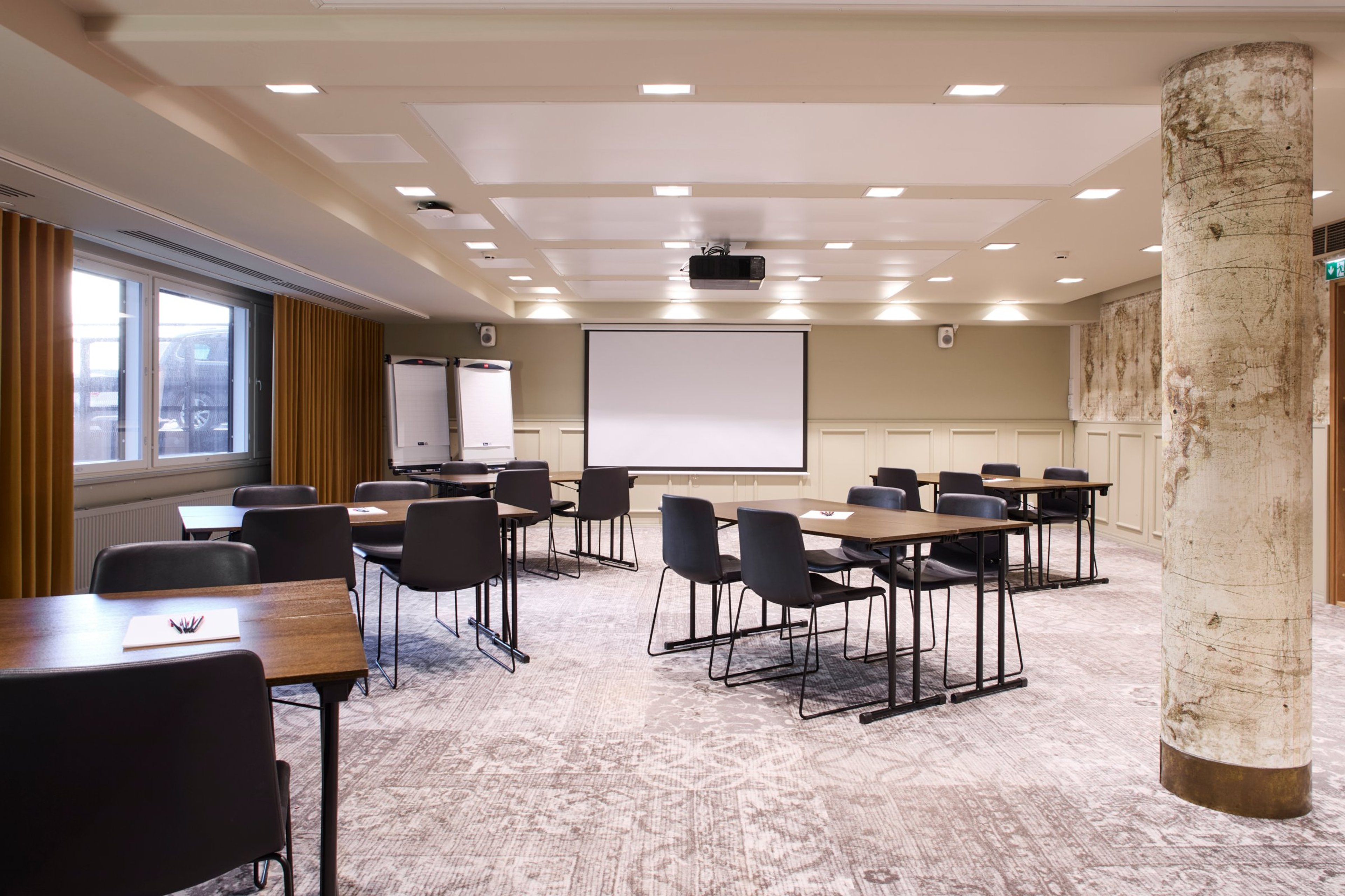 Neuvotteluhuone pöydillä ja tuoleilla, seinällä valkokangas ja fläppitaulut. Tilassa marmorinen pilari ja tasainen kokolattiamatto.