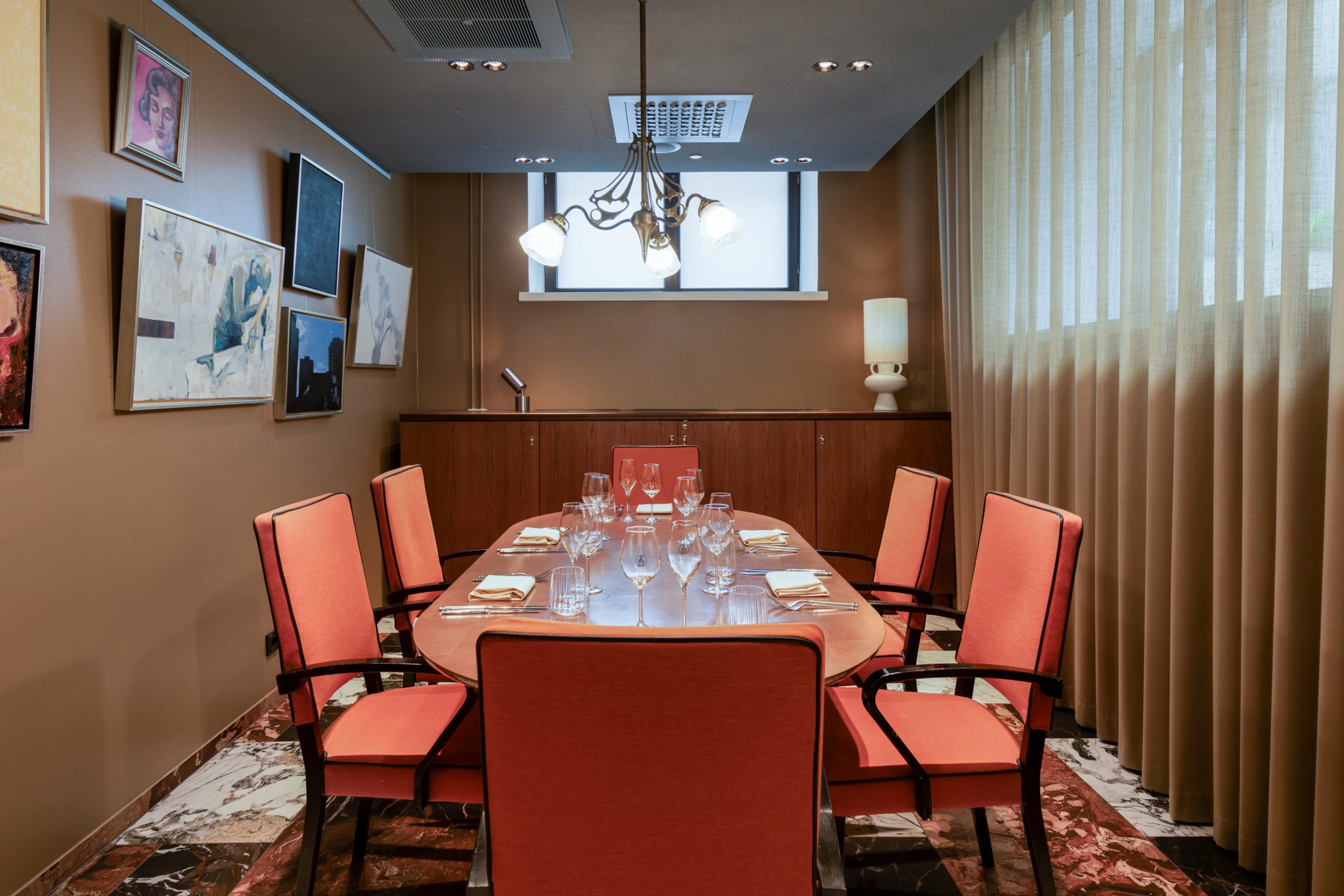 Elegantti neuvotteluhuone, jossa on ovaali pöytä, korallinsävyiset tuolit, marmorilattia, taideteoksia seinillä ja kattokruunu.