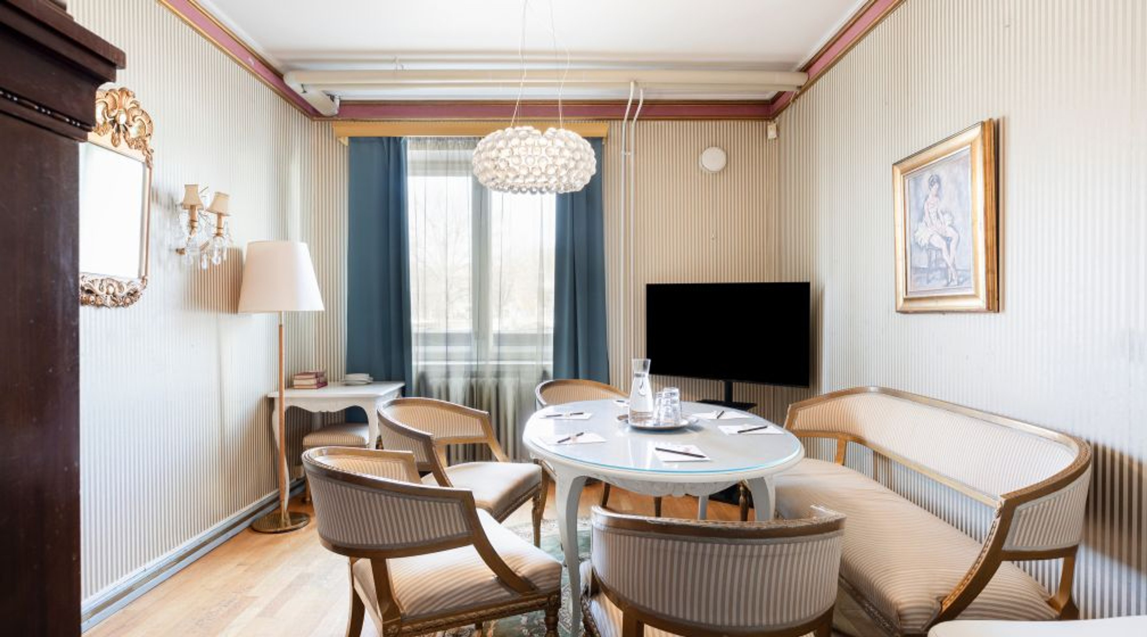Meeting room with round table and chairs, wall-mounted television, and window providing natural light.