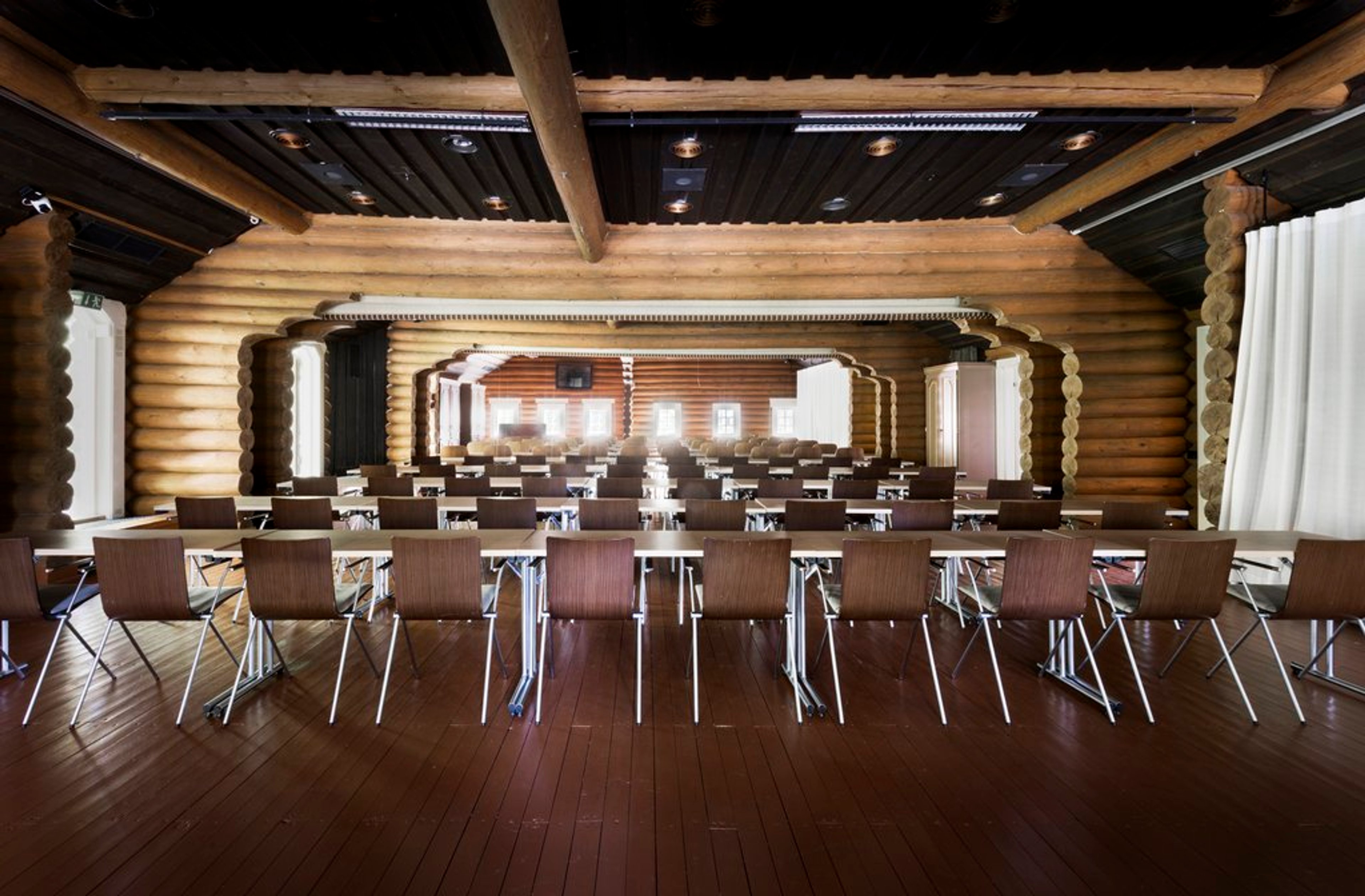 Conference room with log walls, dark wooden flooring and rows of chairs arranged for seating.