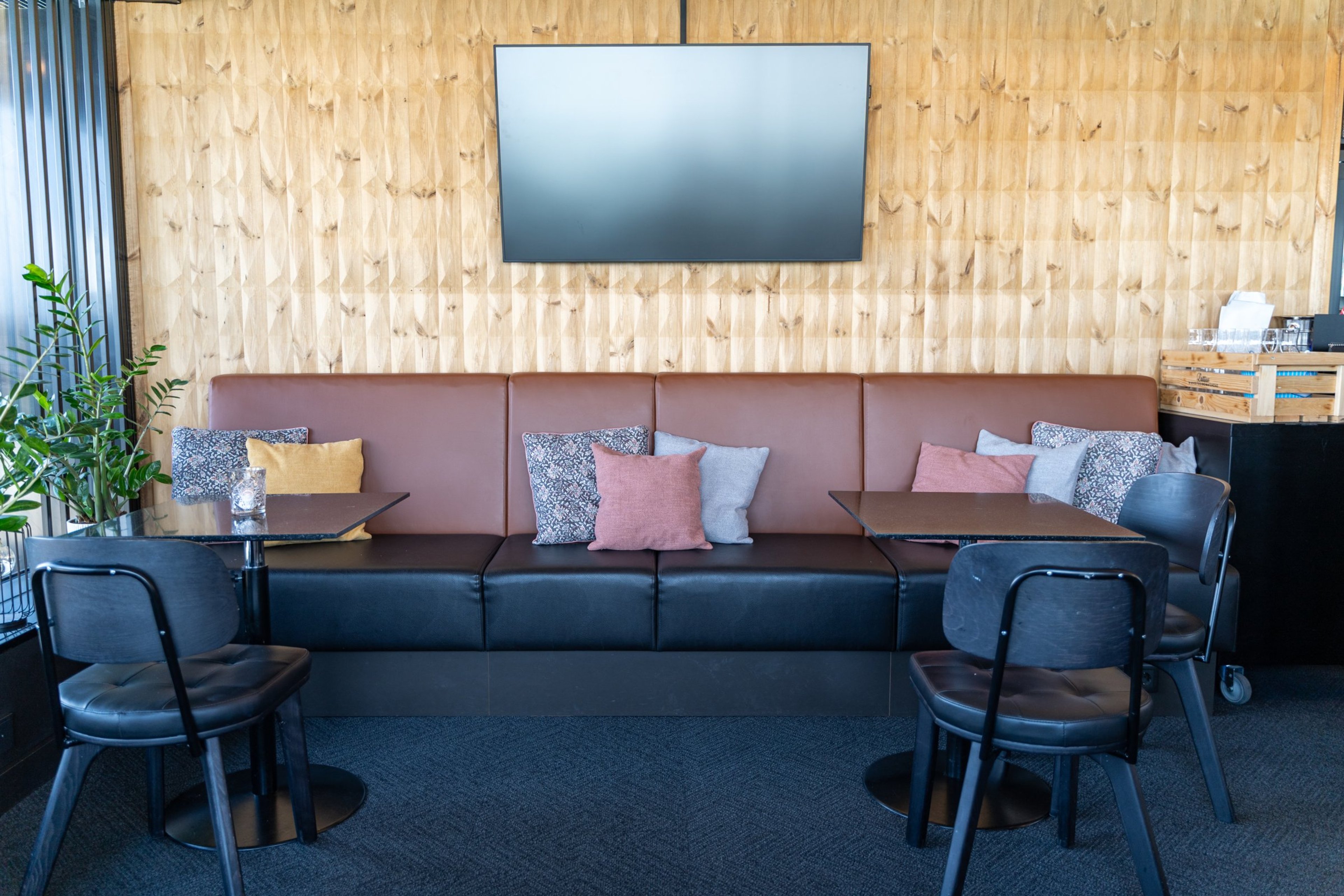 Moderni ravintolatila puisella seinäpaneelilla, ruskea nahkasohva värikkäillä tyynyillä..