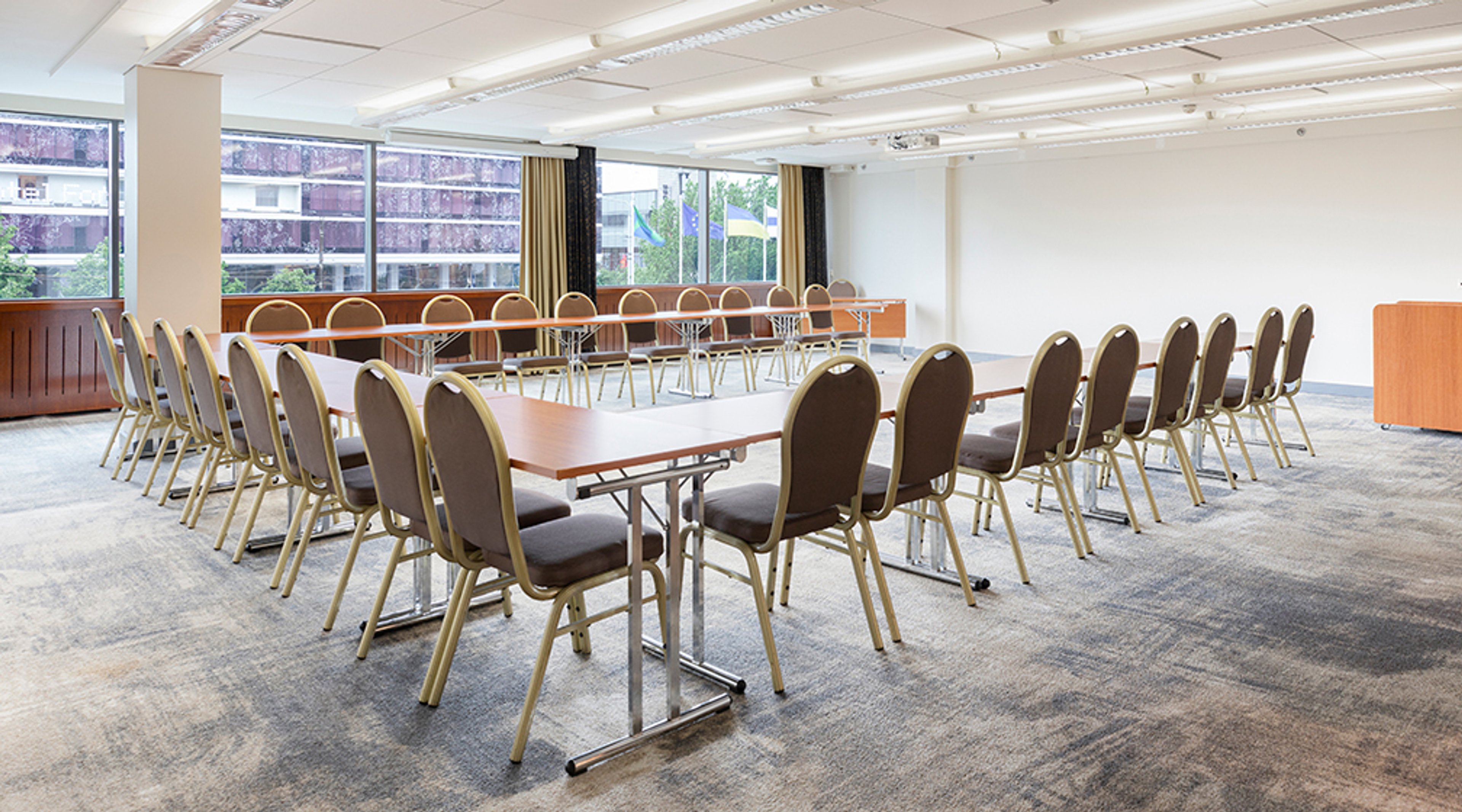 Bright conference room with long tables and upholstered chairs in rows. Space has level access, but floor has low-pile carpeting.