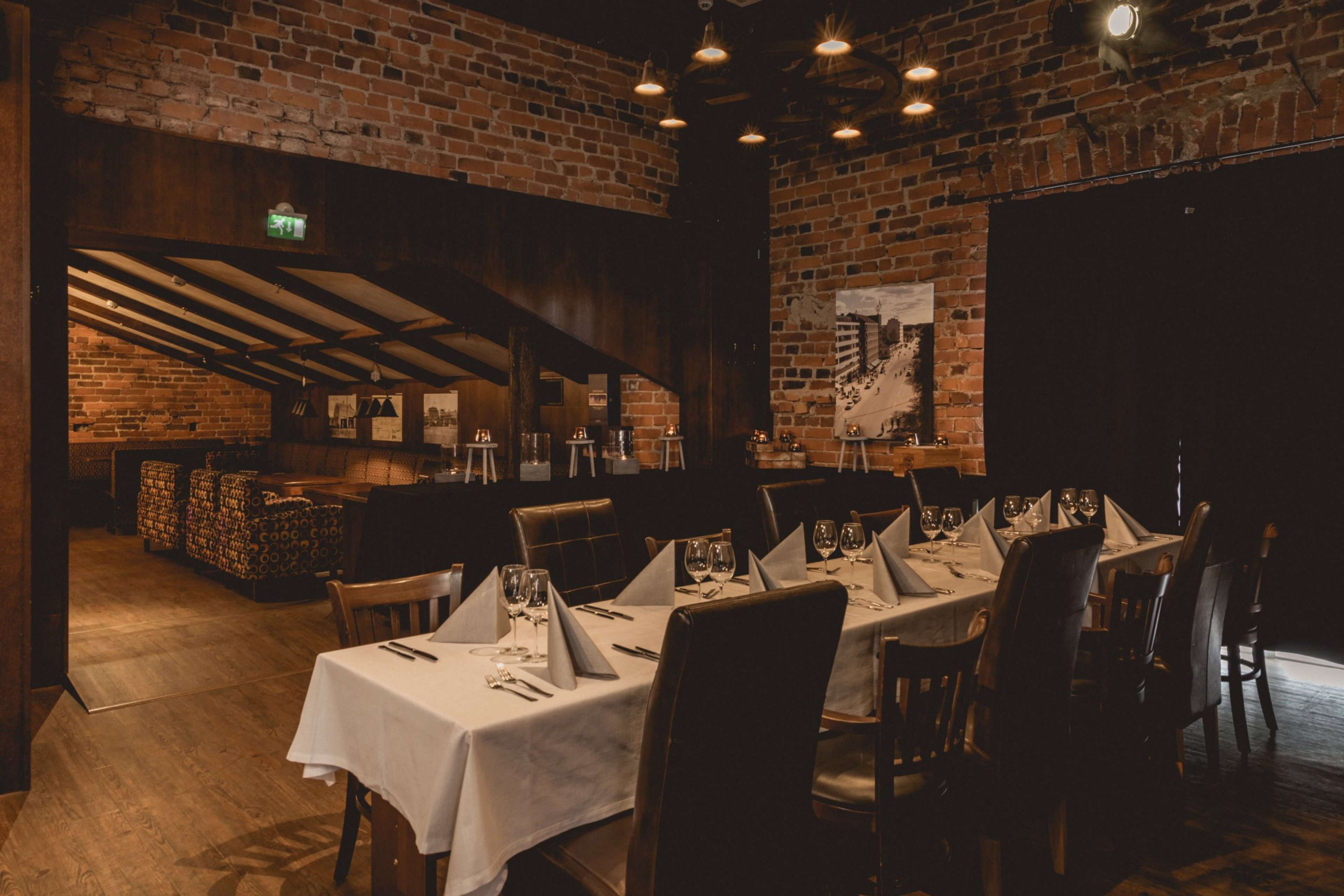 Tunnelmallinen ravintola tiiliseinillä, katossa riippuvat valaisimet, valkoliinaiset pöydät ja puulattia. Taustalla loungealue.