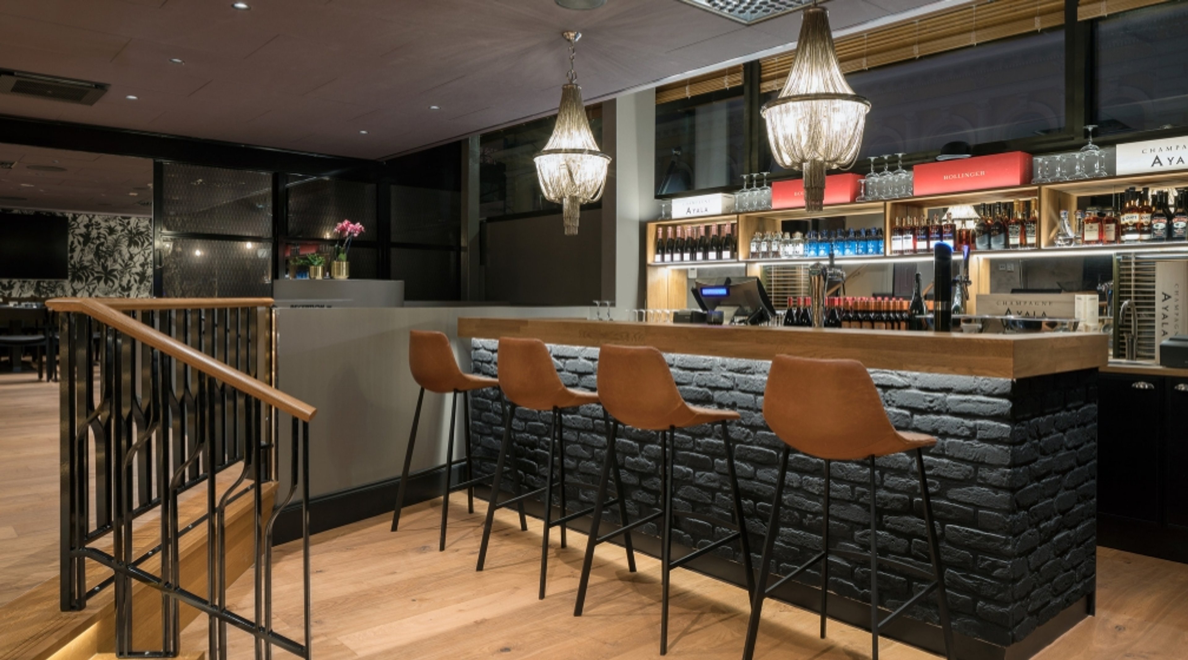 Moderni baari, jossa on musta tiilitiskiosa, oranssinruskeat baarituolit, kristallikruunut ja puulattia.