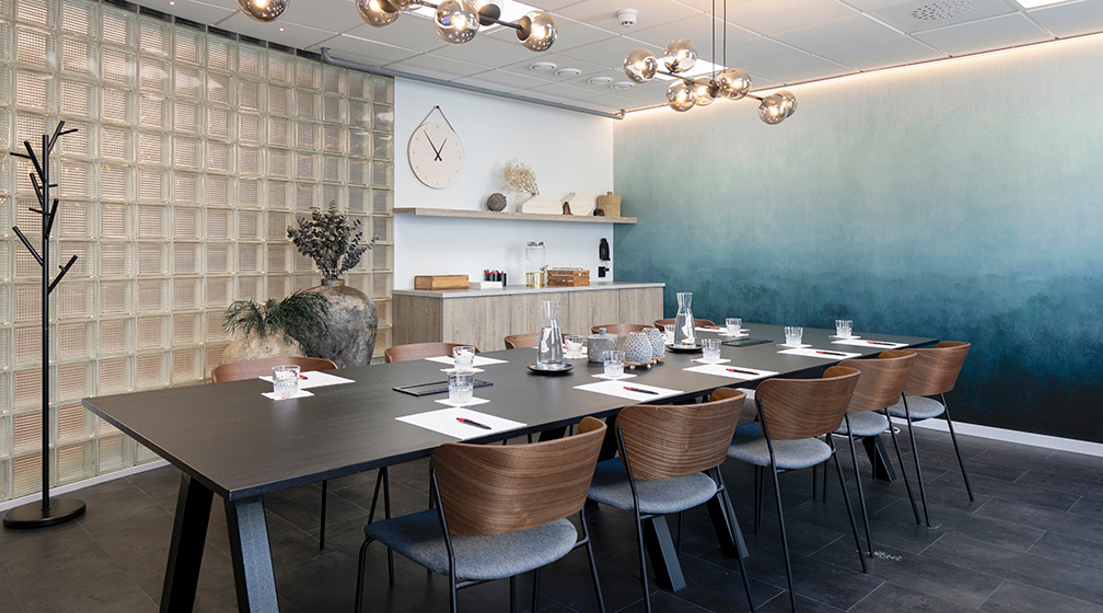 Moderni neuvotteluhuone, jossa tumma pöytä, puiset tuolit, sininen liukuvärjätty seinä ja lasikuutioseinä. Valaisimet riippuvat katosta.