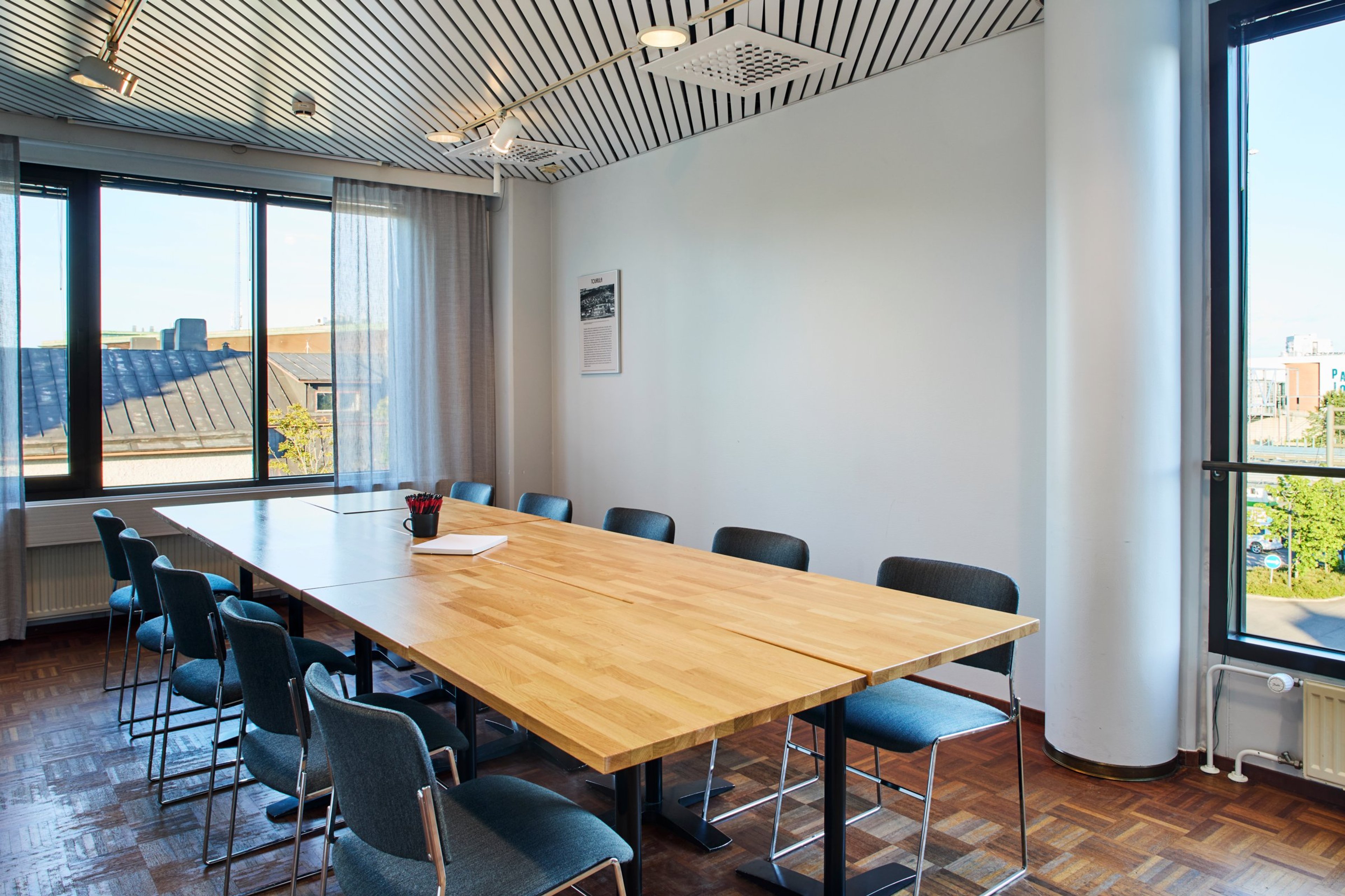 Valoisa neuvotteluhuone puisella pöydällä ja sinisillä tuoleilla. Suuret ikkunat, puulattia ja raidallinen katto.