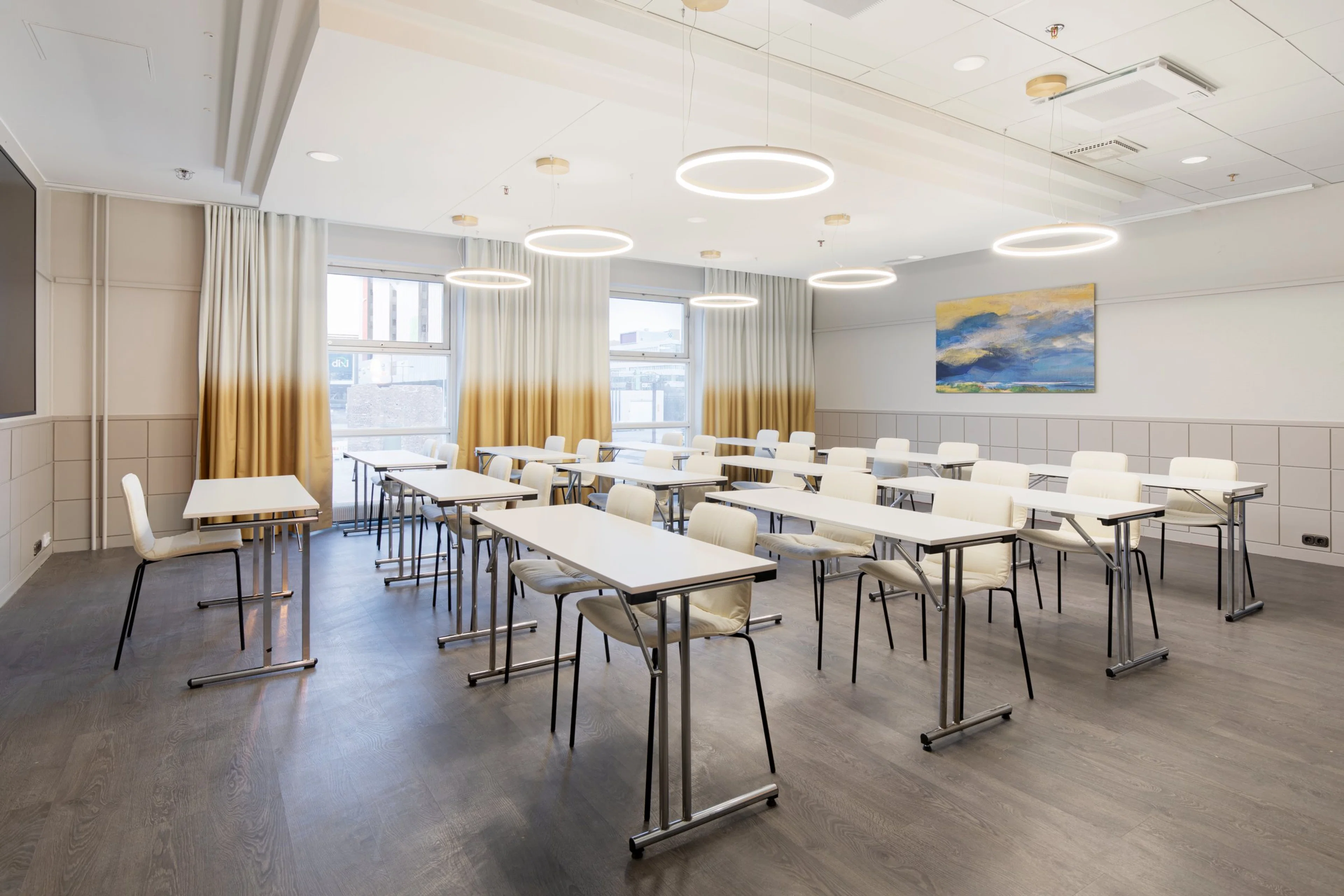 Moderni kokoustila valkoisilla pöydillä ja tuoleilla. Katto-ombré-verhot ikkunoilla, ympyrämäiset valaisimet ja tasainen puulattia.