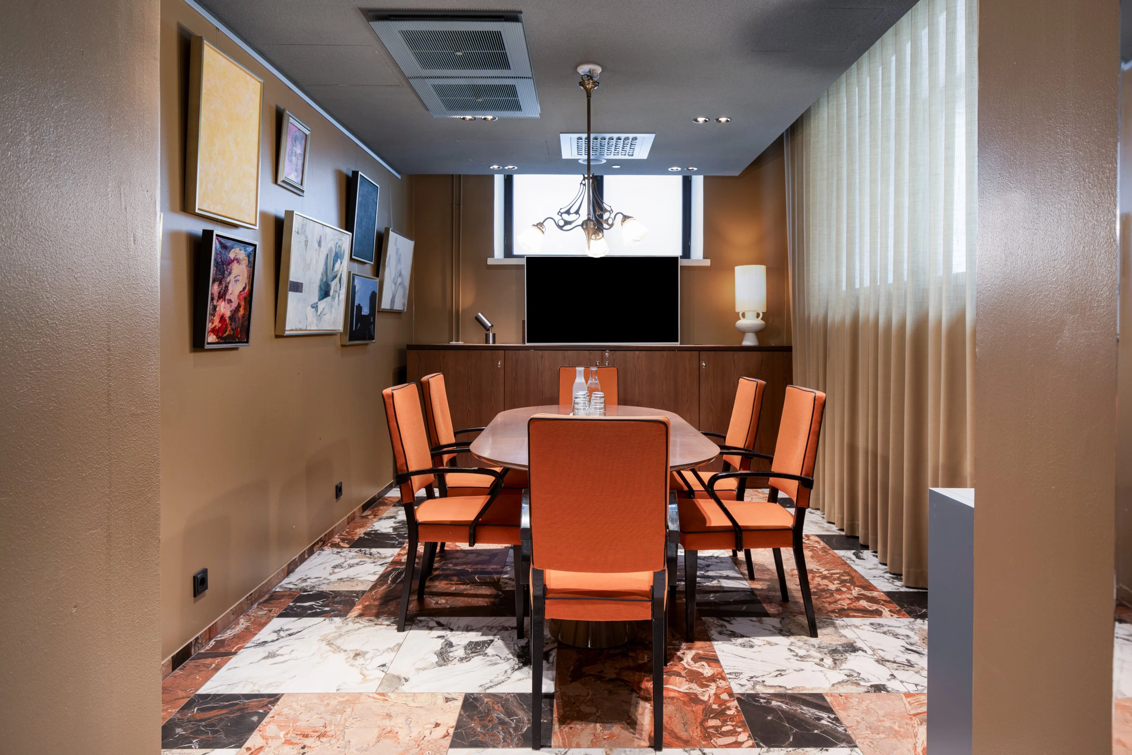 Neuvotteluhuone, jossa oranssi tuolit ovaalin pöydän ympärillä, marmorilattia, tauluja seinällä ja esitysnäyttö edessä.