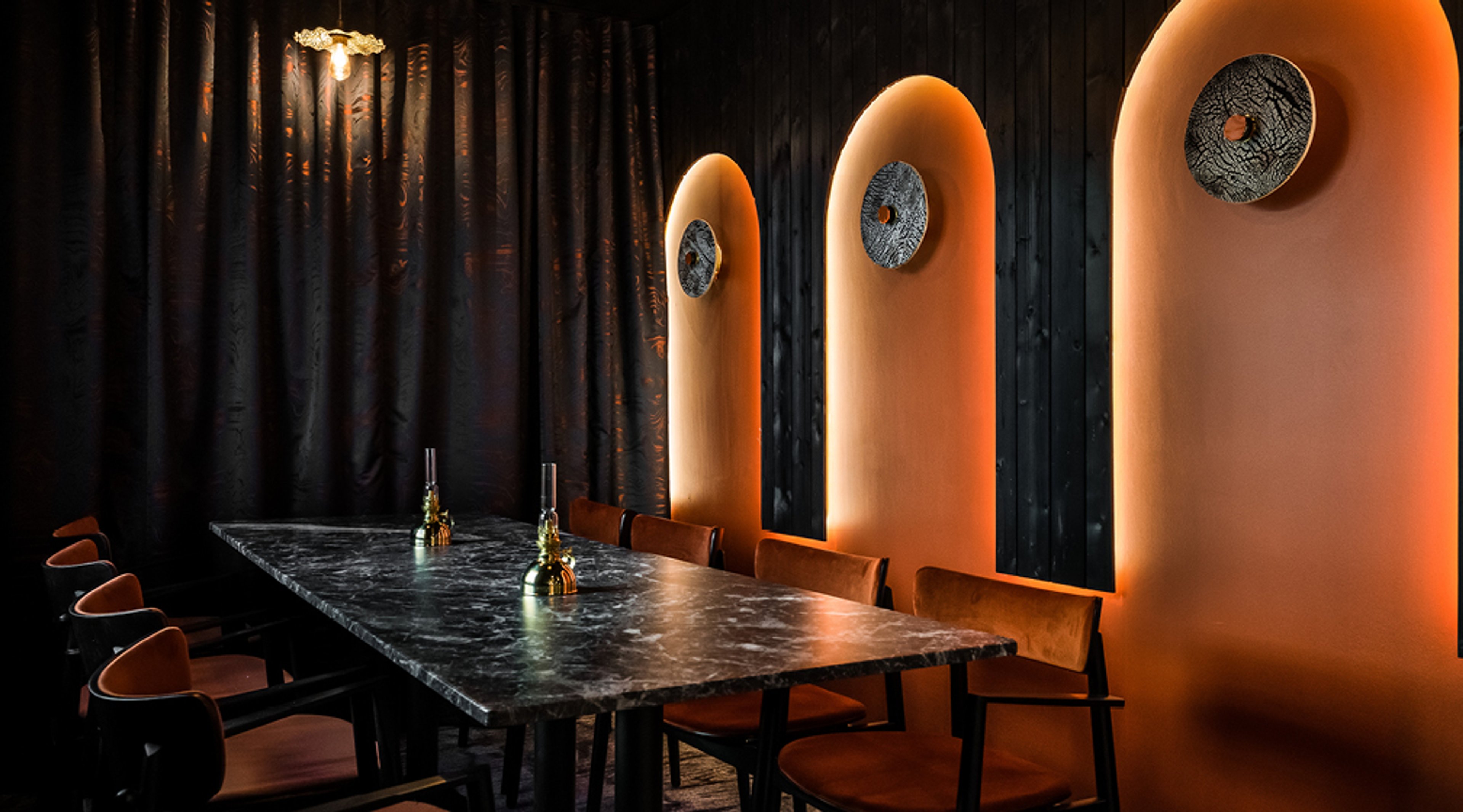 Tyylikäs ravintolan seurusteluhuone, jossa musta marmorikuvioinen pöytä ja ruskeita tuoleja.