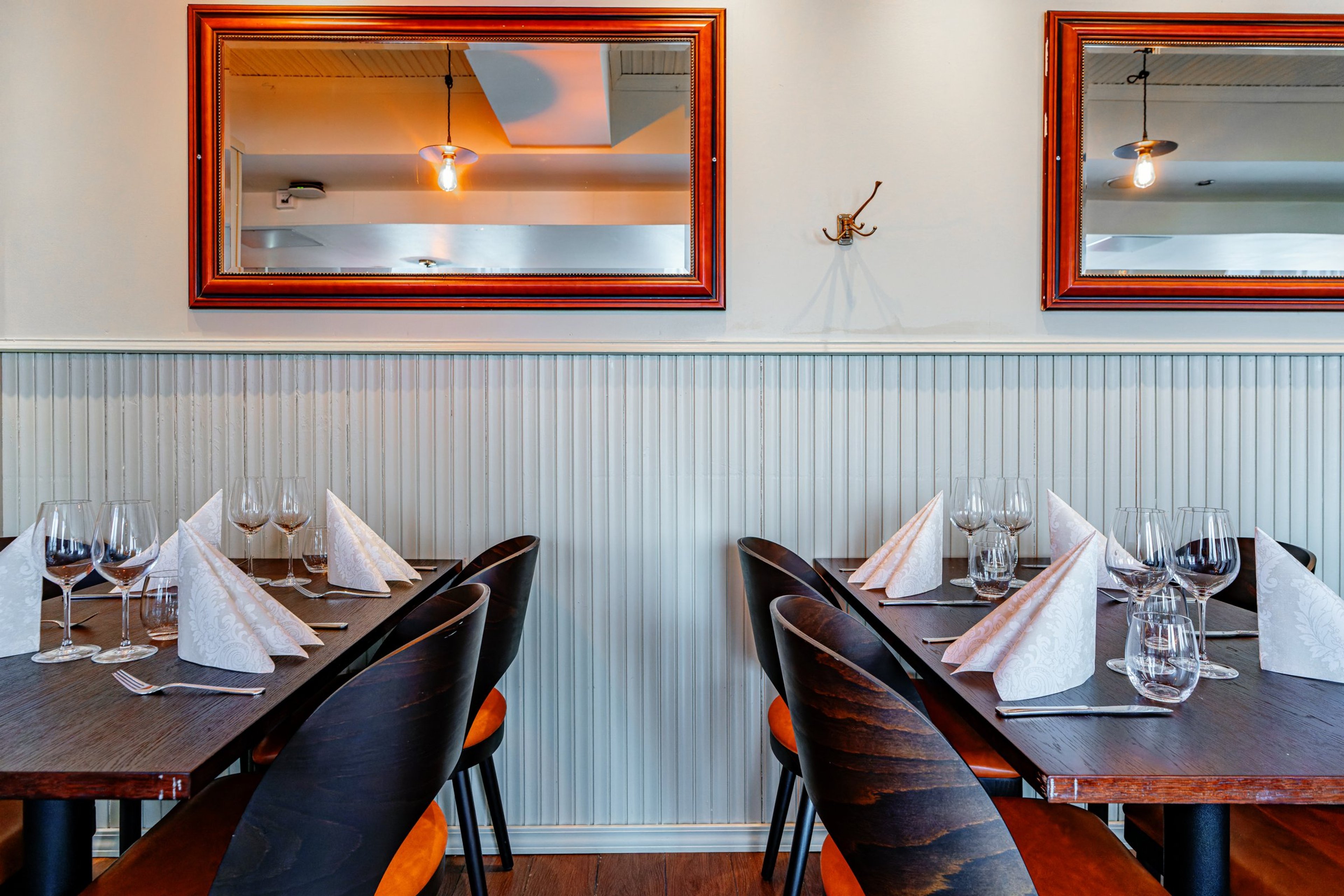 Ravintolan sisustus, jossa pöydät on katettu viinilaseilla ja lautasliinoilla. Seinällä on puukehyksiset peilit ja paneeliseinä.