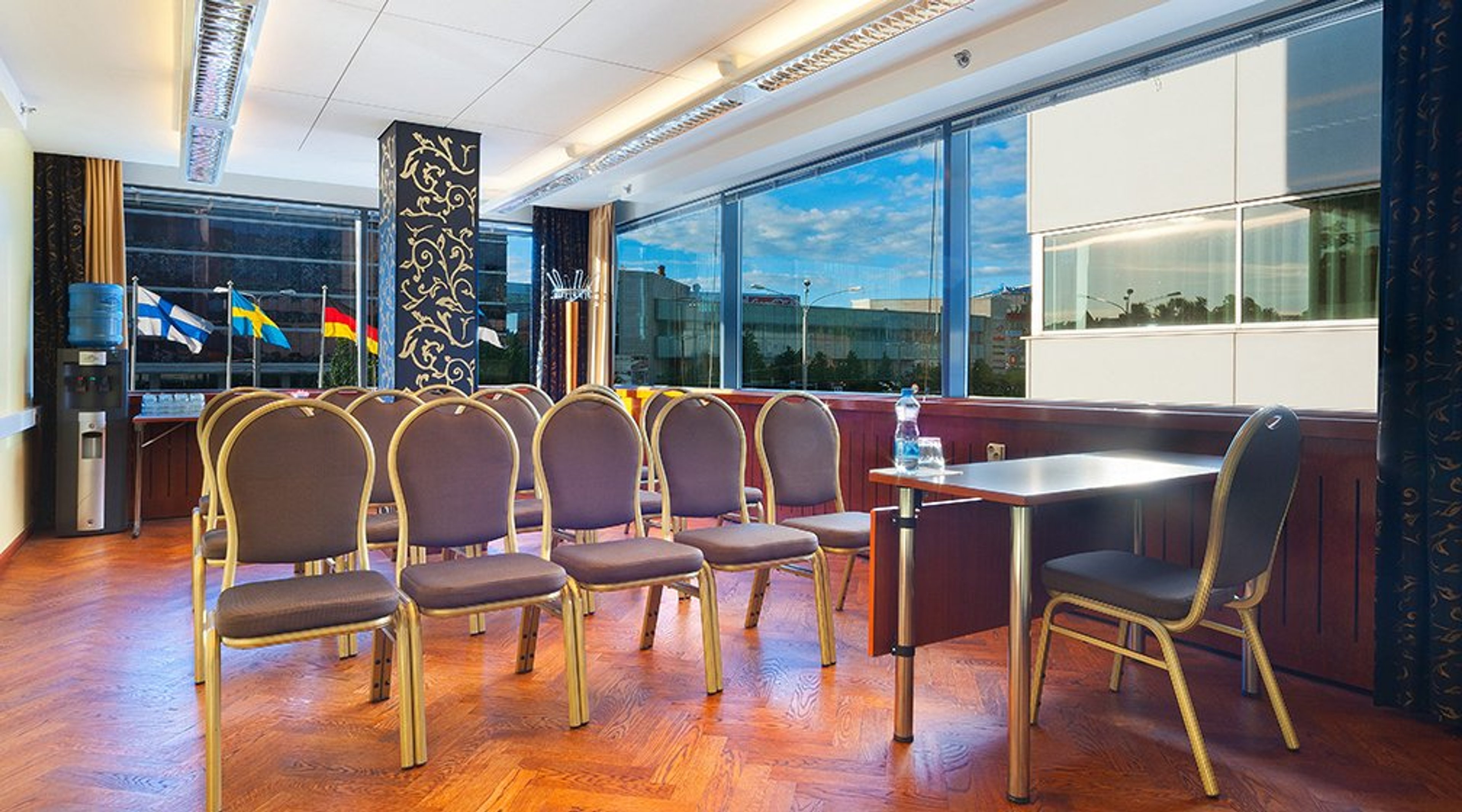 Neuvotteluhuone puuparkettilattioilla ja violeteilla tuoleilla. Suurista ikkunoista avautuu näkymä ulos, jossa näkyy lippuja ja kaupunkimaisemaa.