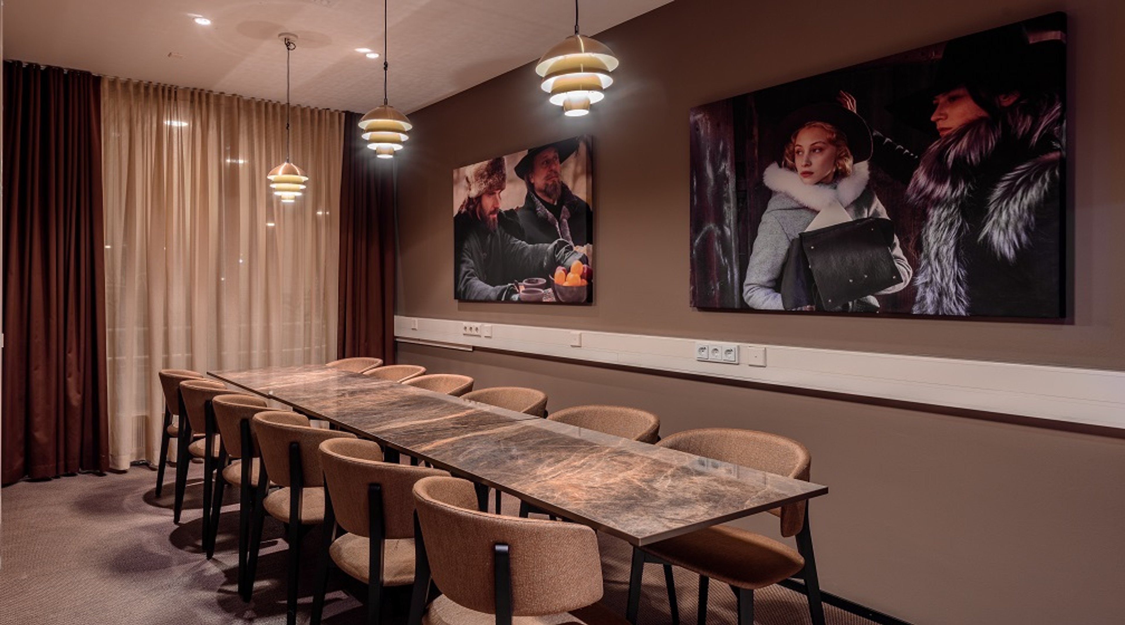 Moderni neuvotteluhuone marmorikansisellla pöydällä, pehmeillä tuoleilla ja tyylikkäillä riippuvalaisimilla. Ruskeat seinät ja valokuvataidetta.