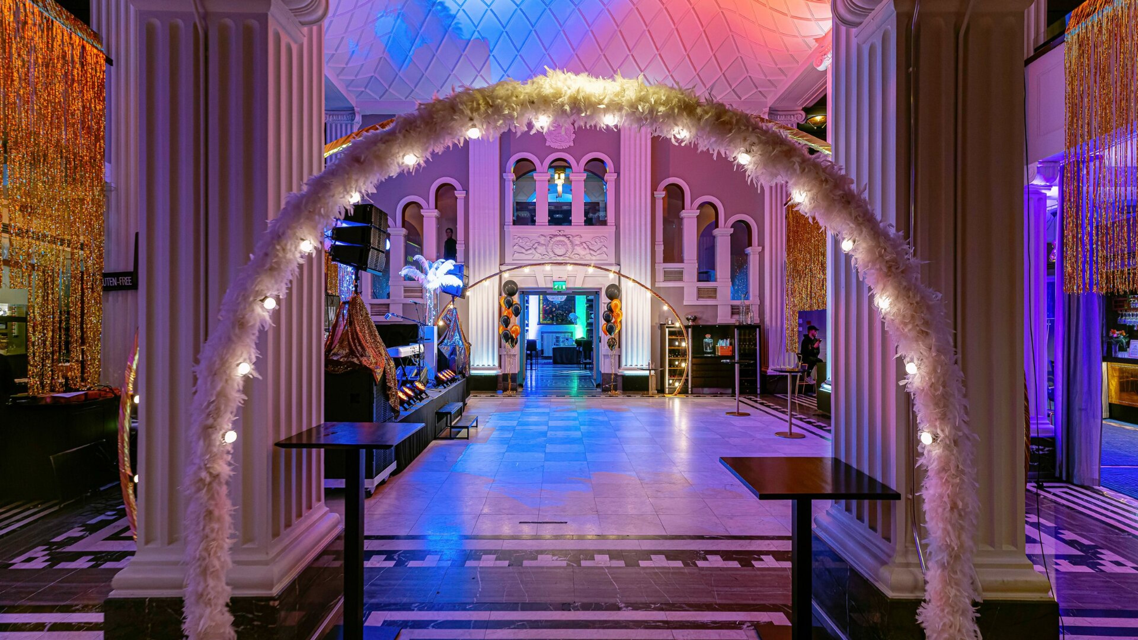 Koristeellinen tapahtumapaikka valkoisilla pylväillä, valaistulla kaarella ja kuvioidulla kivilattialla. Avara sisäänkäynti ilman portaita.